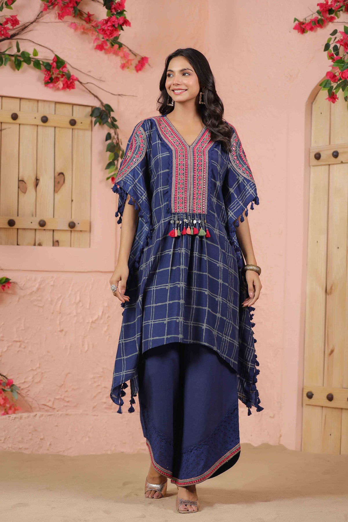Woman wearing a blue traditional outfit with red patterns against a pink wall.