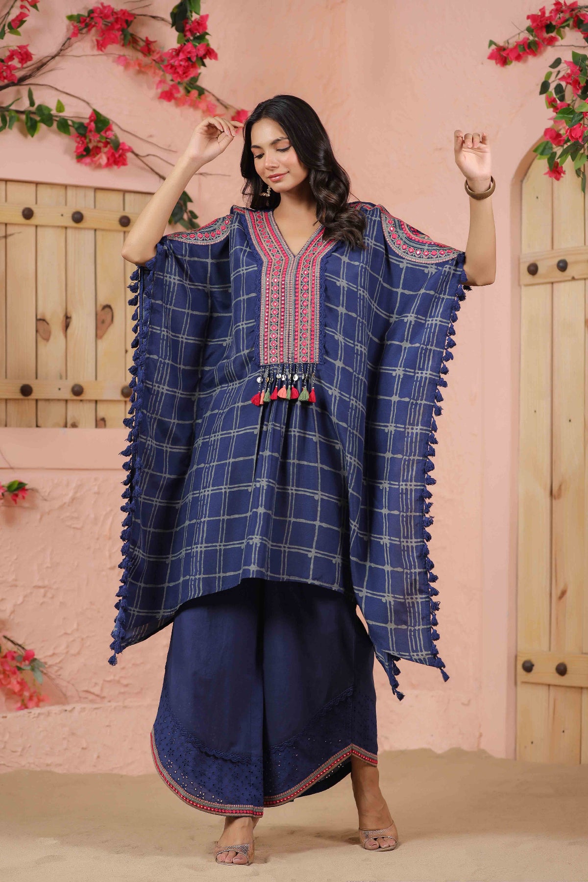 Woman wearing a blue traditional outfit with decorative elements against a pink floral background
