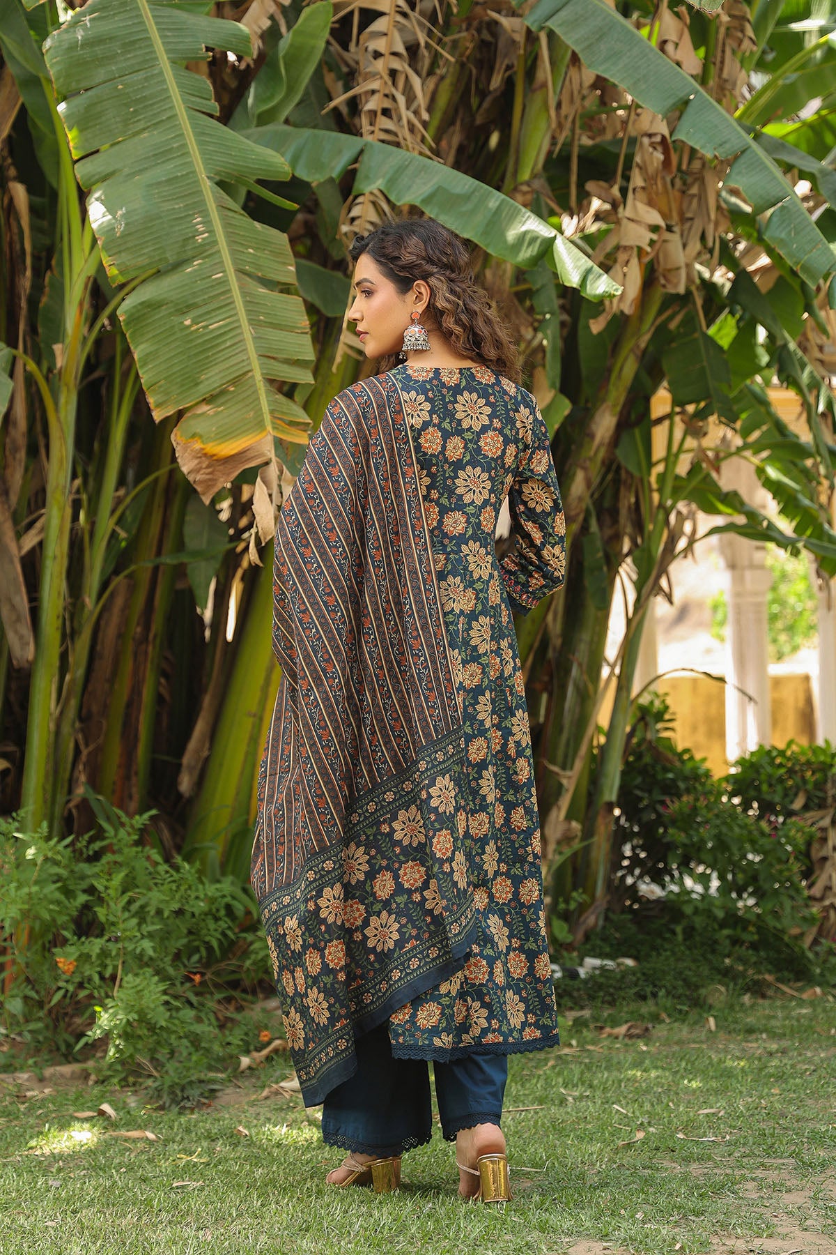 Woman wearing a floral patterned dress standing in a garden with large green leaves.