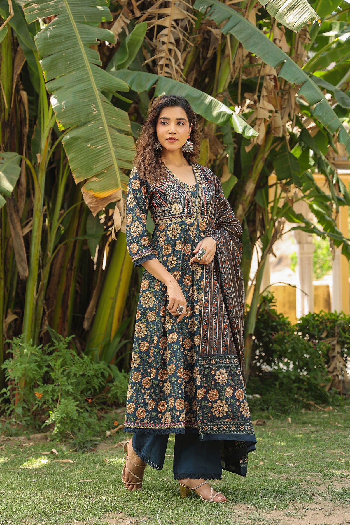 Woman in a patterned dress standing in a garden with large green leaves.