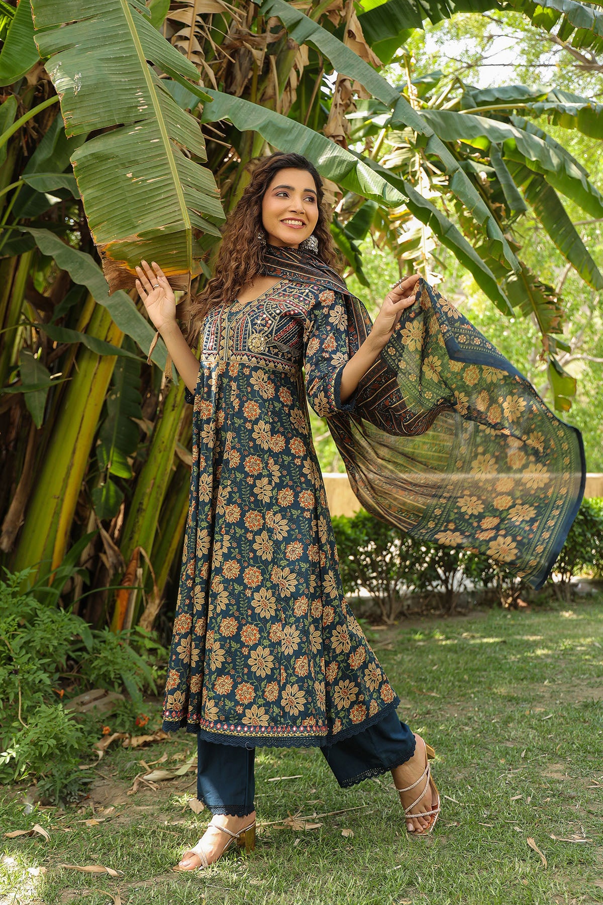 Woman in a floral dress holding a dupatta in a garden setting