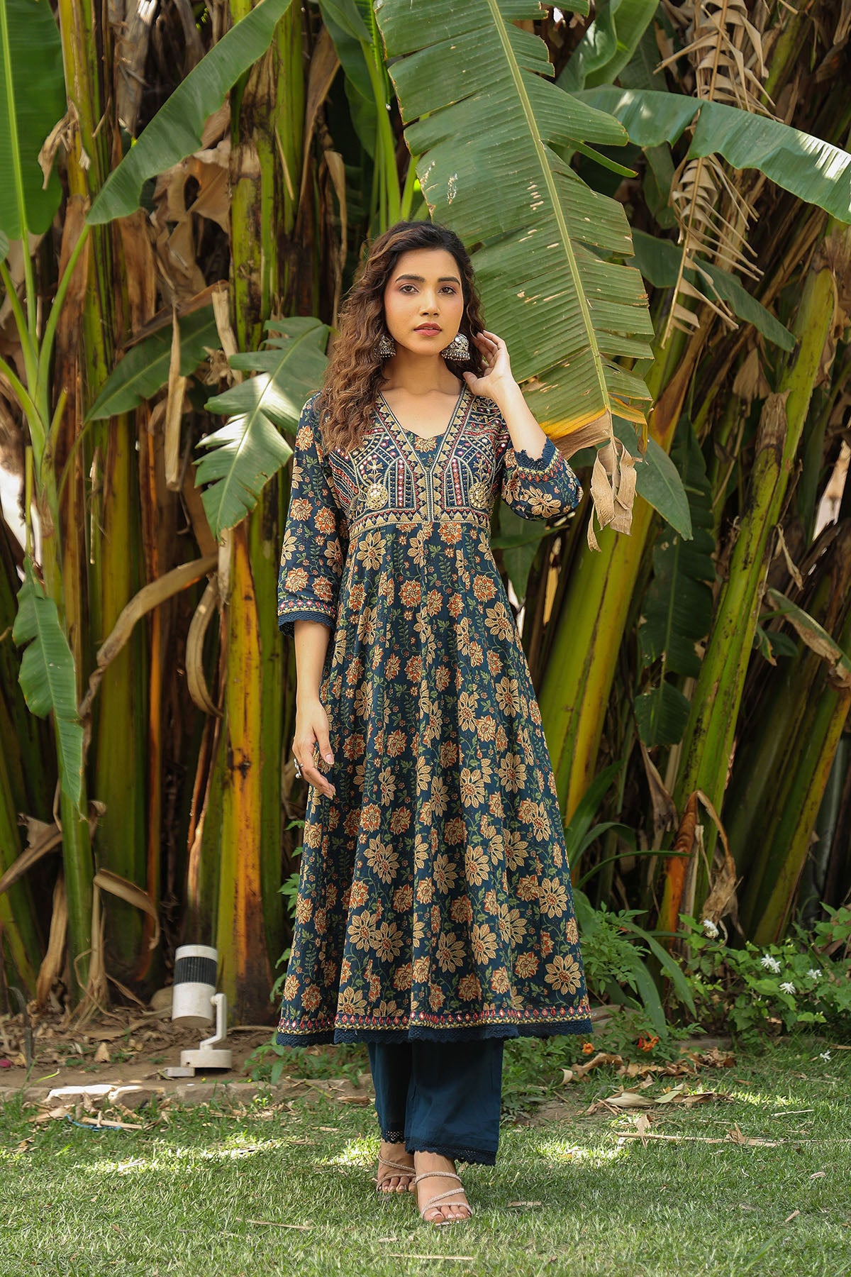 Woman in a floral dress standing in front of large green leaves