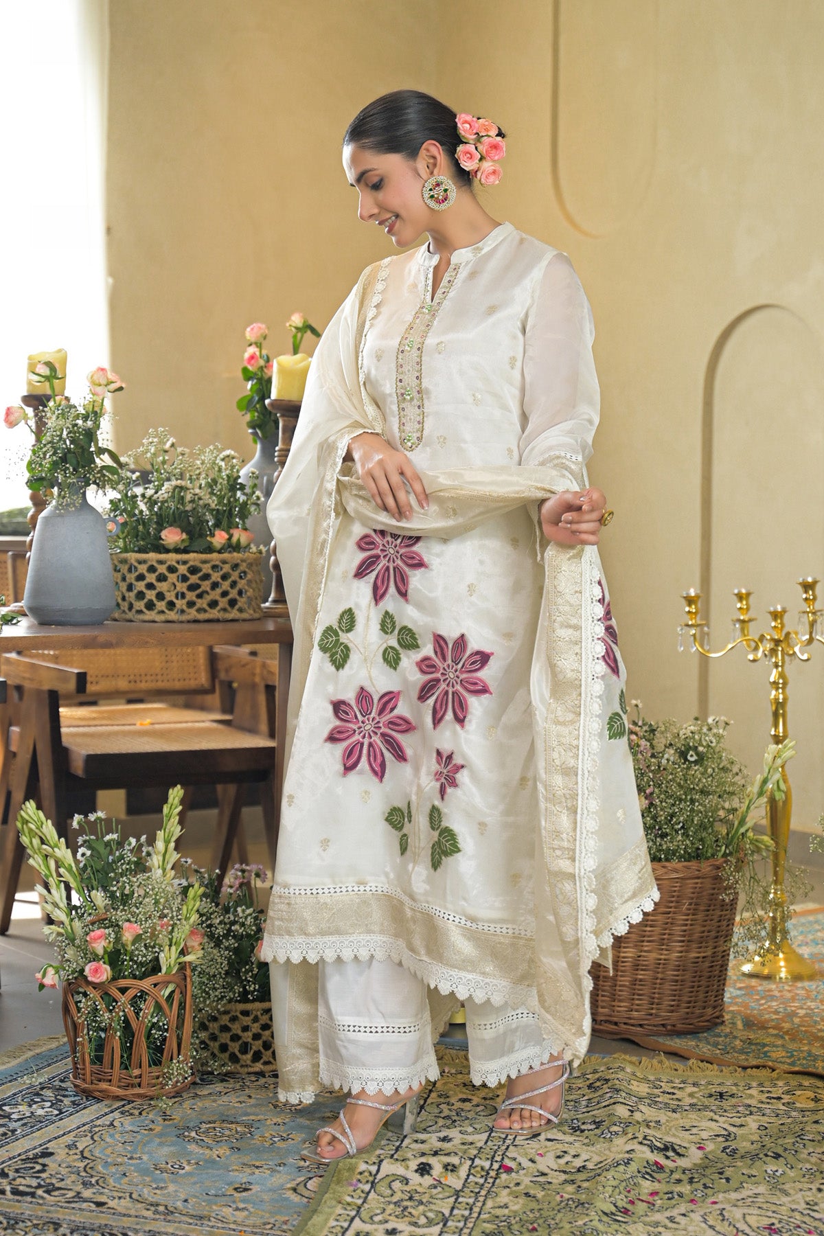 Woman in a white traditional outfit with floral patterns in a decorated room.