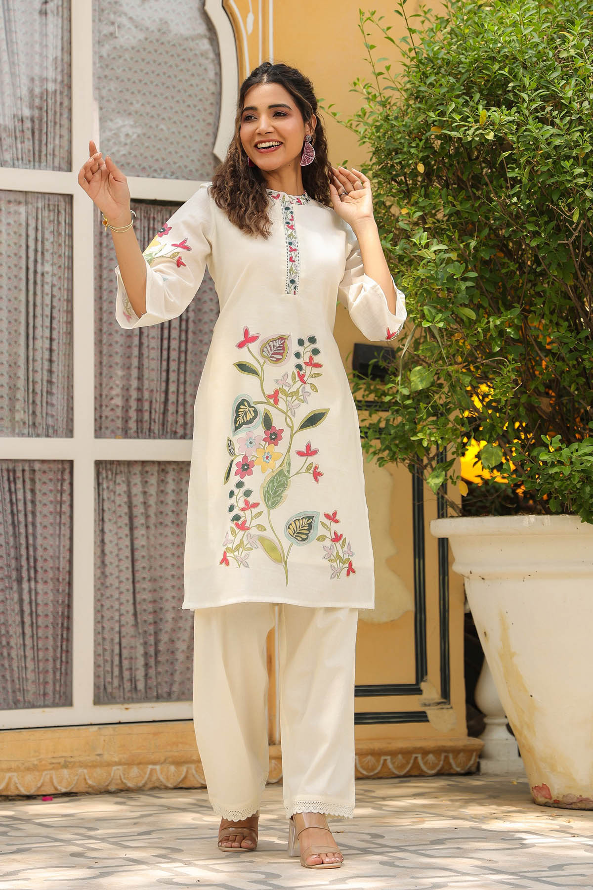Woman wearing a white embroidered kurta with floral patterns in an outdoor setting.