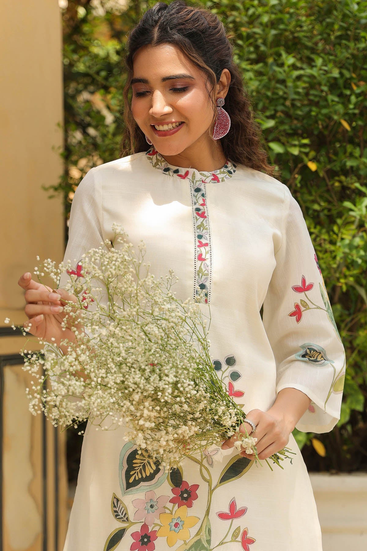 Woman in a white embroidered outfit holding flowers with a blurred green background