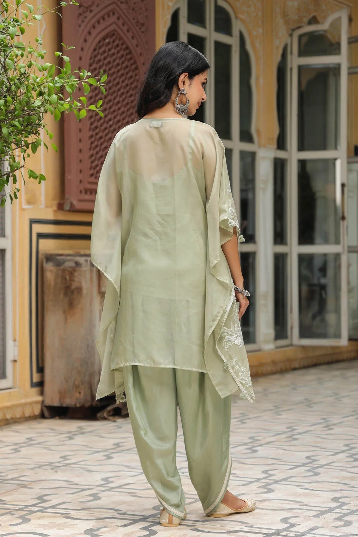 Woman in a light green traditional outfit standing in front of a decorative building entrance.