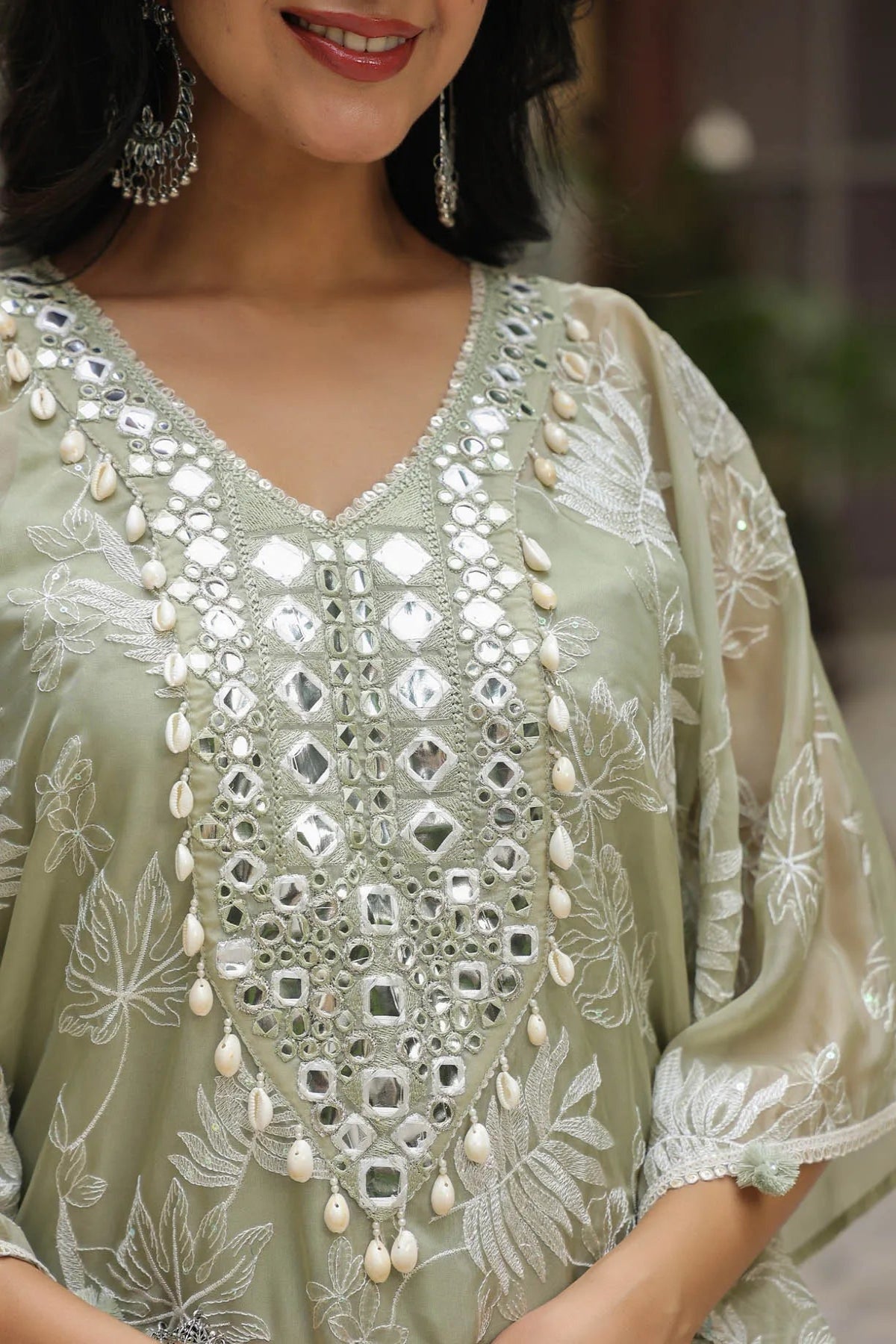 Woman wearing a light green embroidered dress with pearl embellishments.
