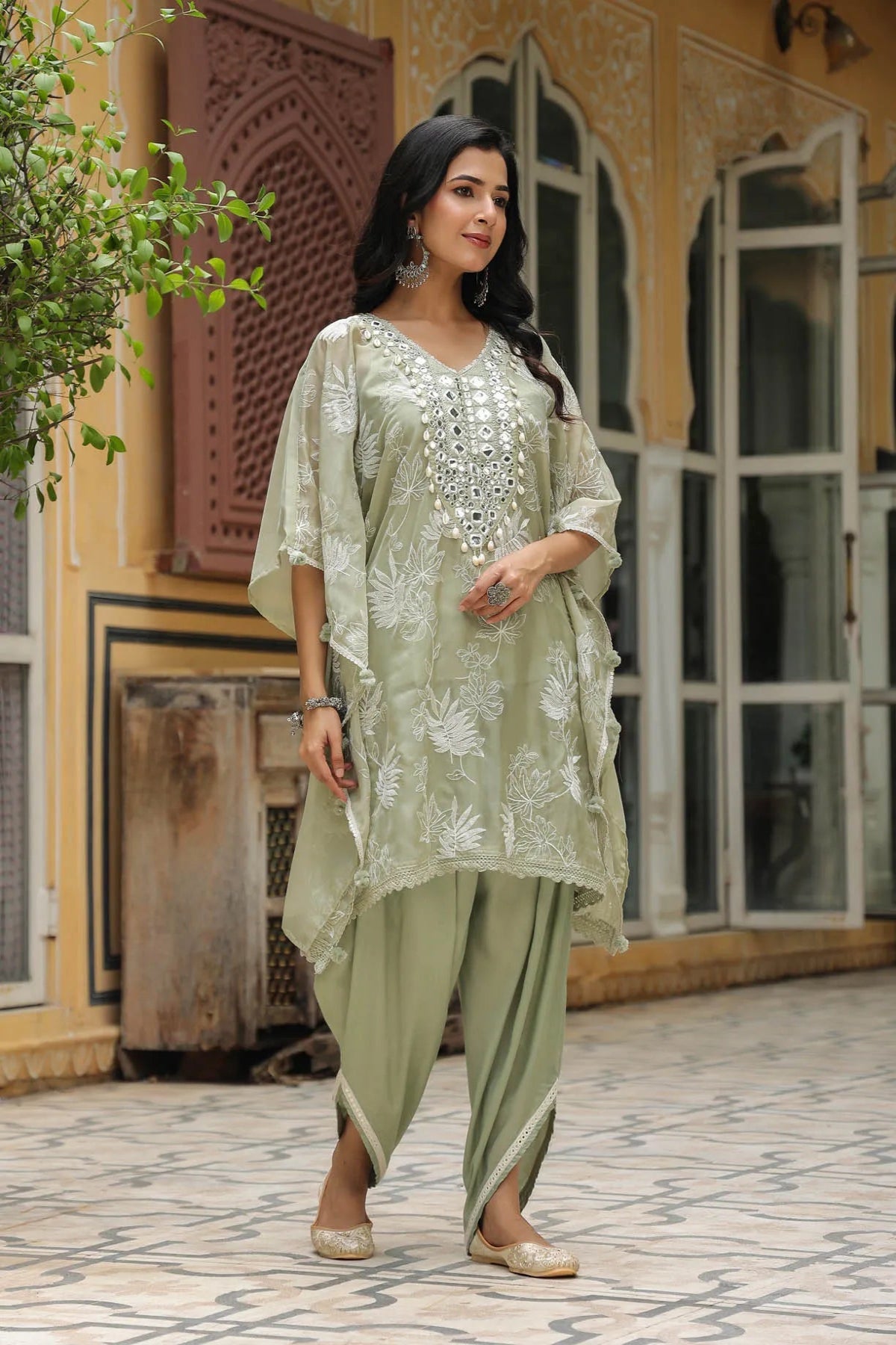 Woman in a light green traditional outfit standing in front of a decorative building.