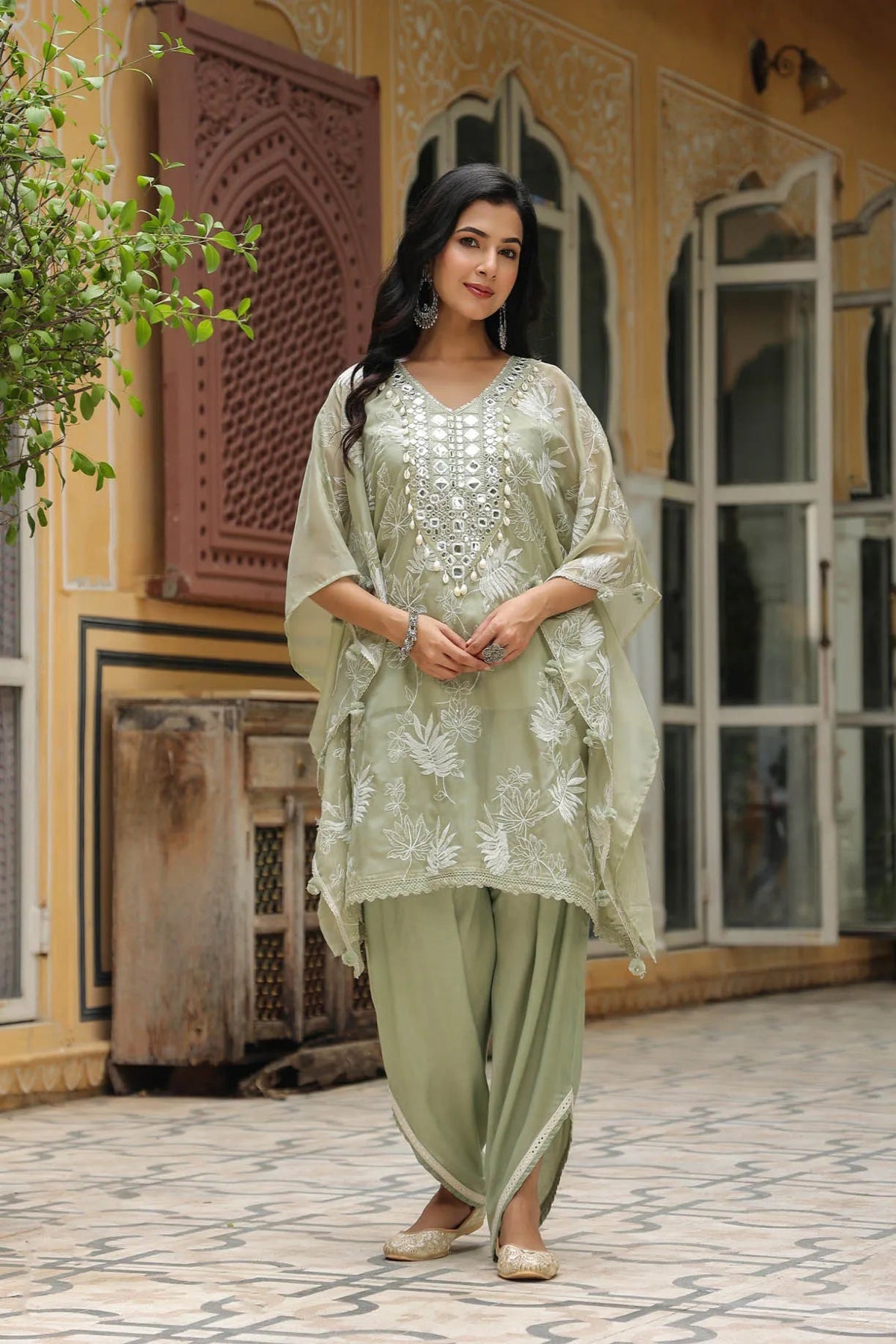 Woman in traditional light green outfit standing in a decorative outdoor setting.