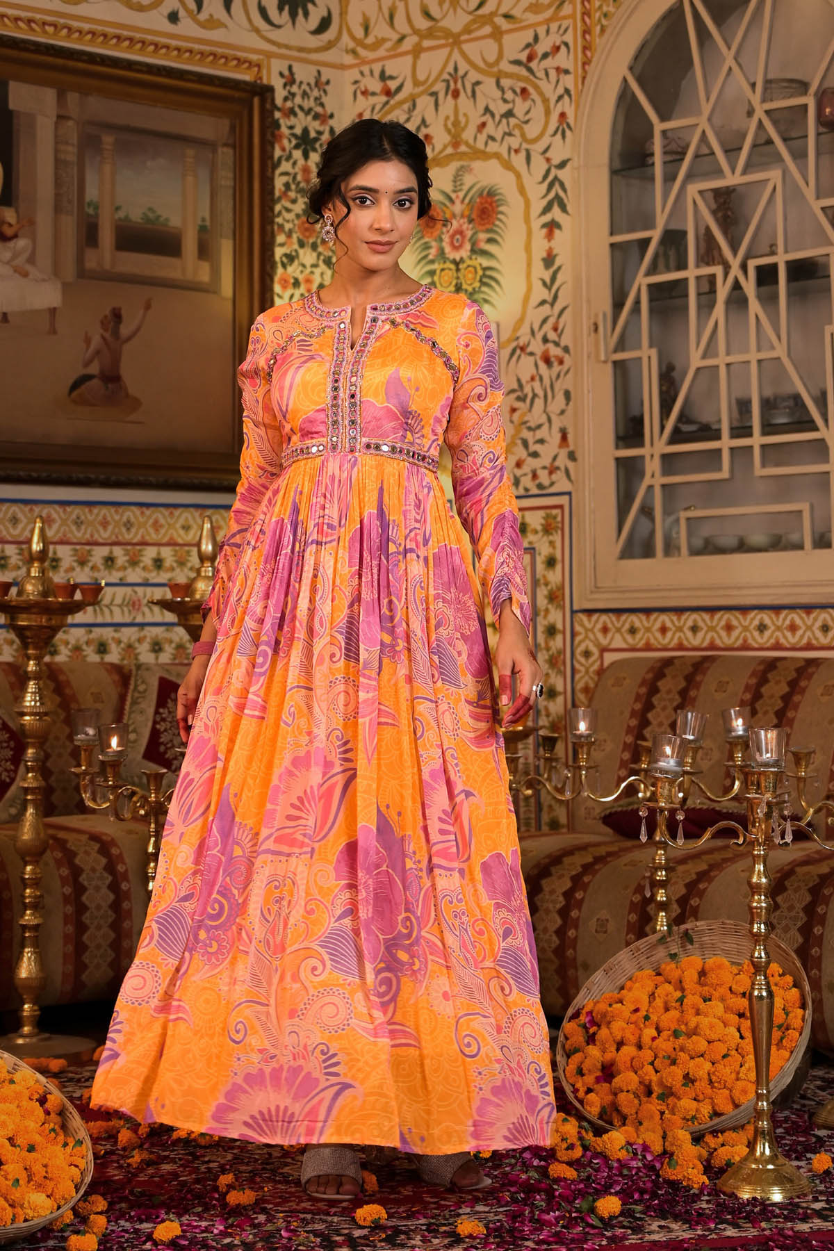 Woman in a vibrant orange and pink dress standing in an ornate room with decorative elements.