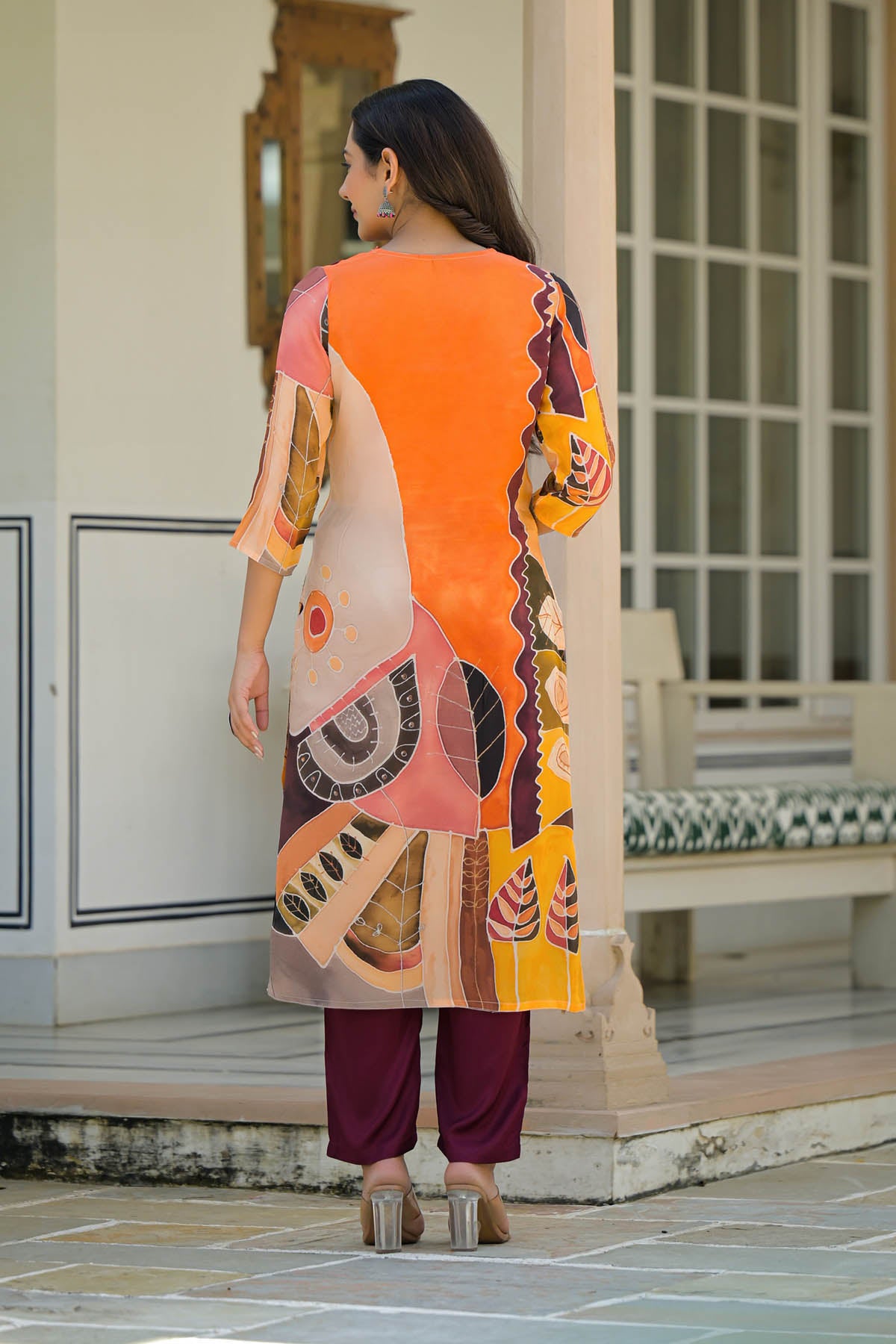 Woman wearing a colorful traditional outfit with a geometric pattern, standing on a stone path.