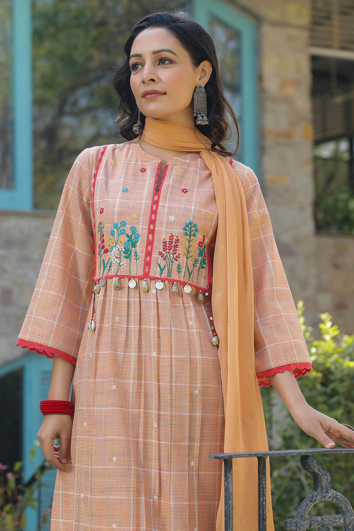 Woman wearing a peach-colored traditional outfit with floral embroidery and a matching dupatta.