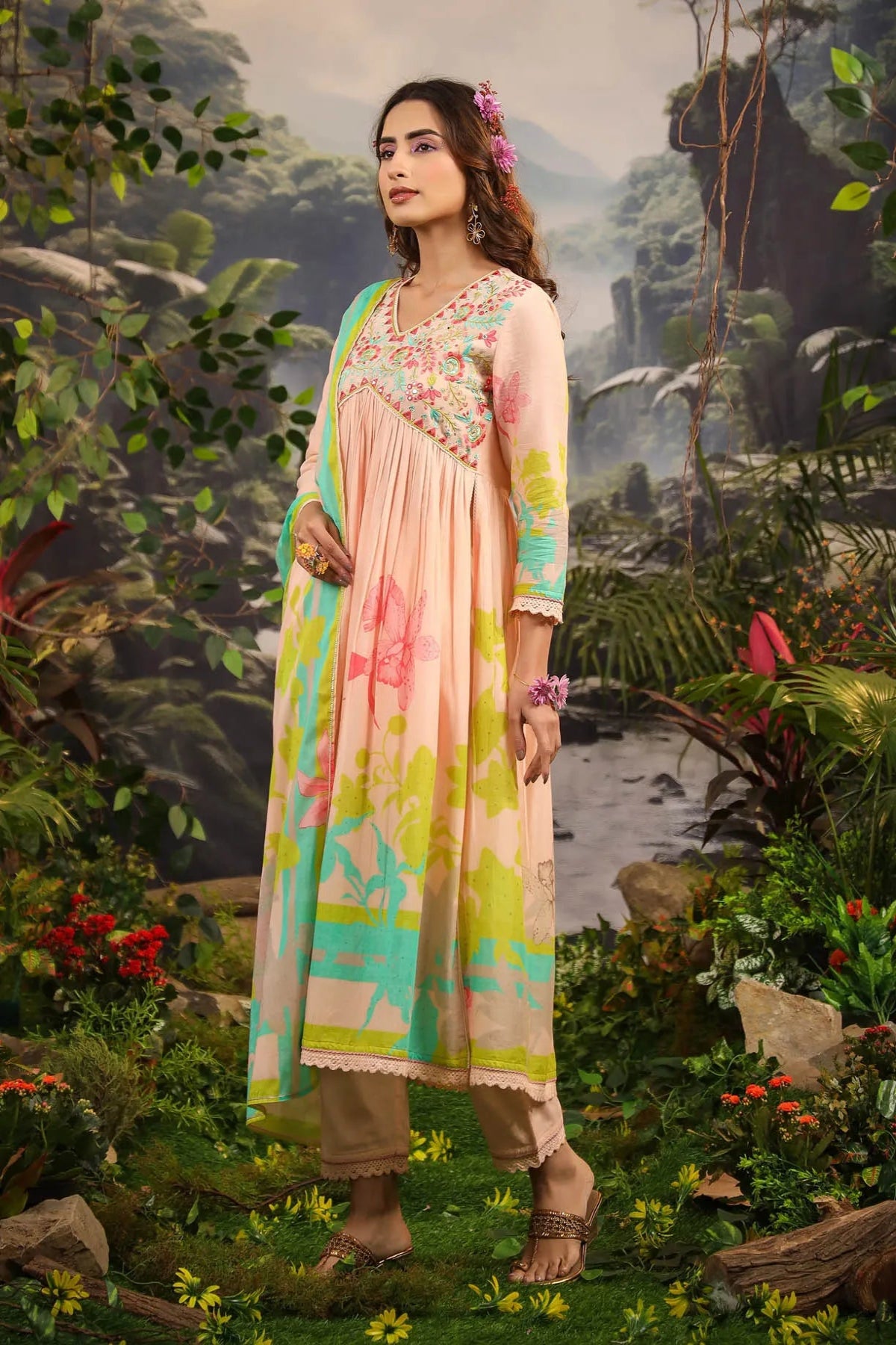 Woman in a colorful traditional outfit standing in a lush, tropical setting.