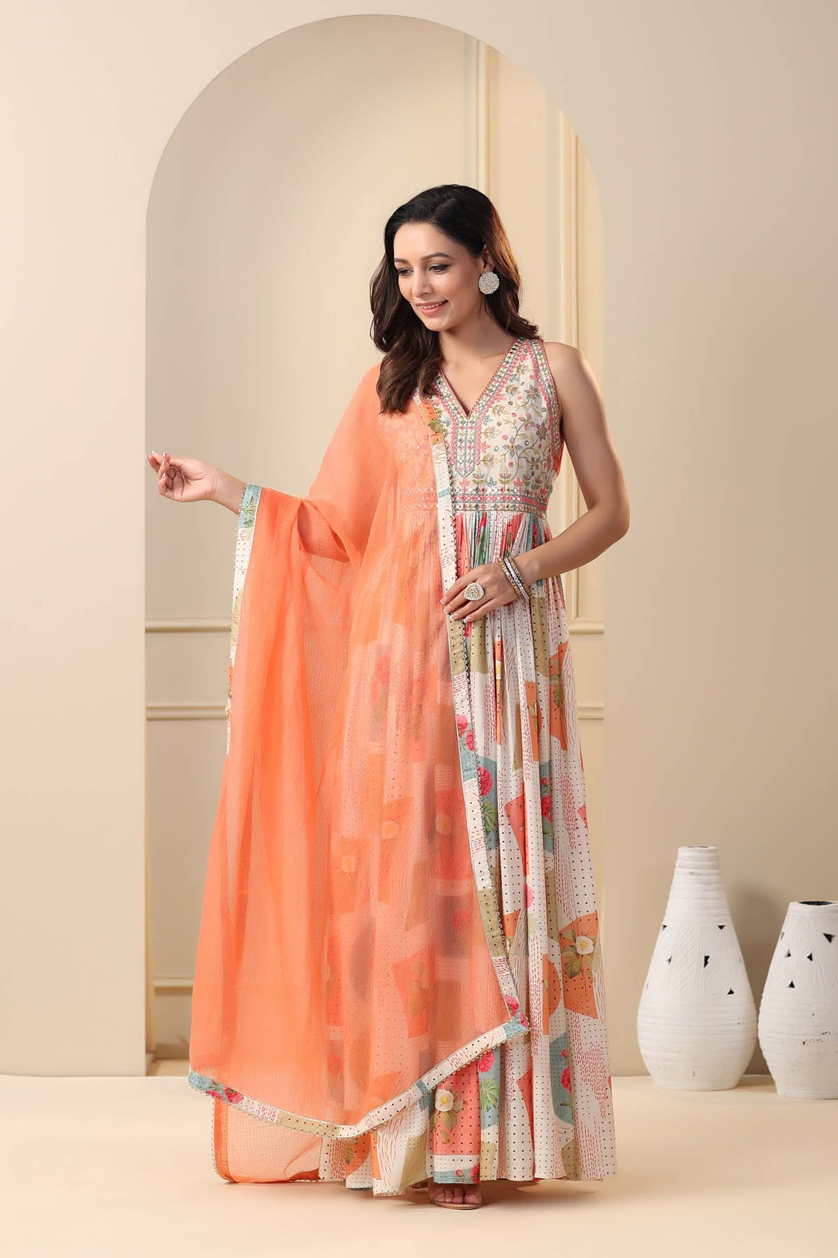 Woman wearing a traditional outfit with an orange dupatta in a minimalistic setting