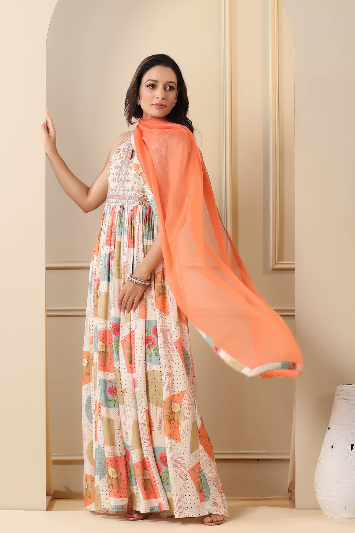 Woman wearing a floral dress with an orange dupatta in a neutral setting