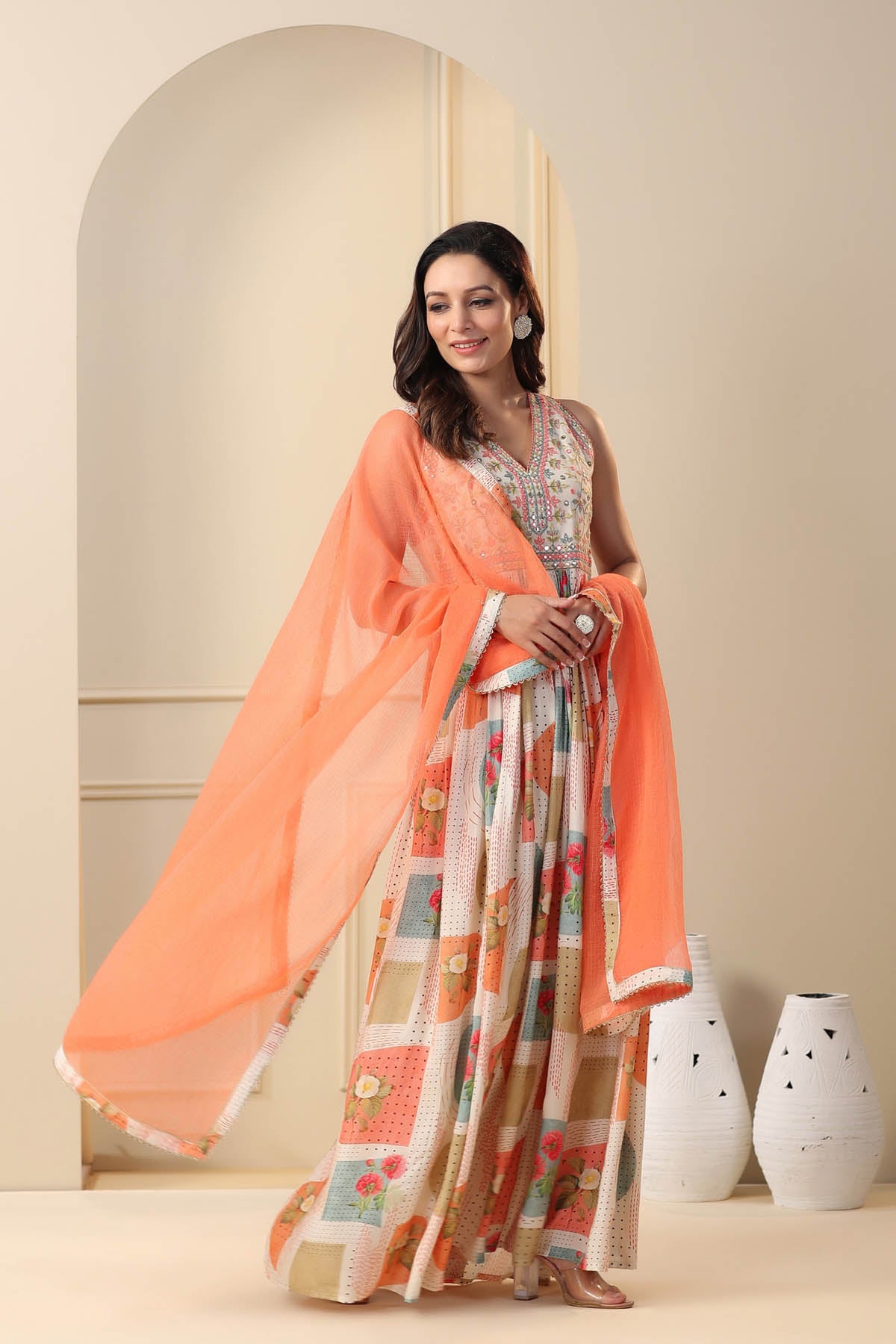 Woman wearing an orange dupatta over a patterned outfit in a minimalistic setting.