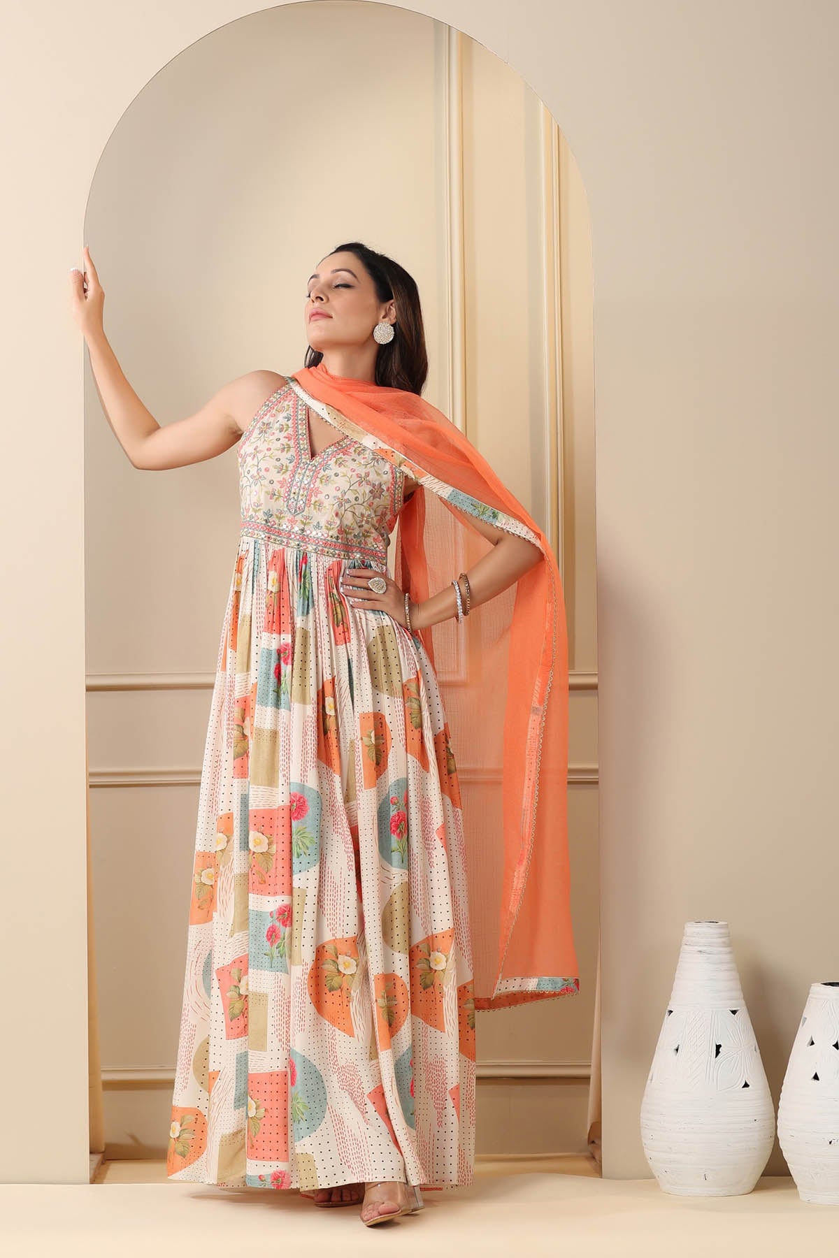 Woman in a floral dress with an orange dupatta standing in front of a mirror.