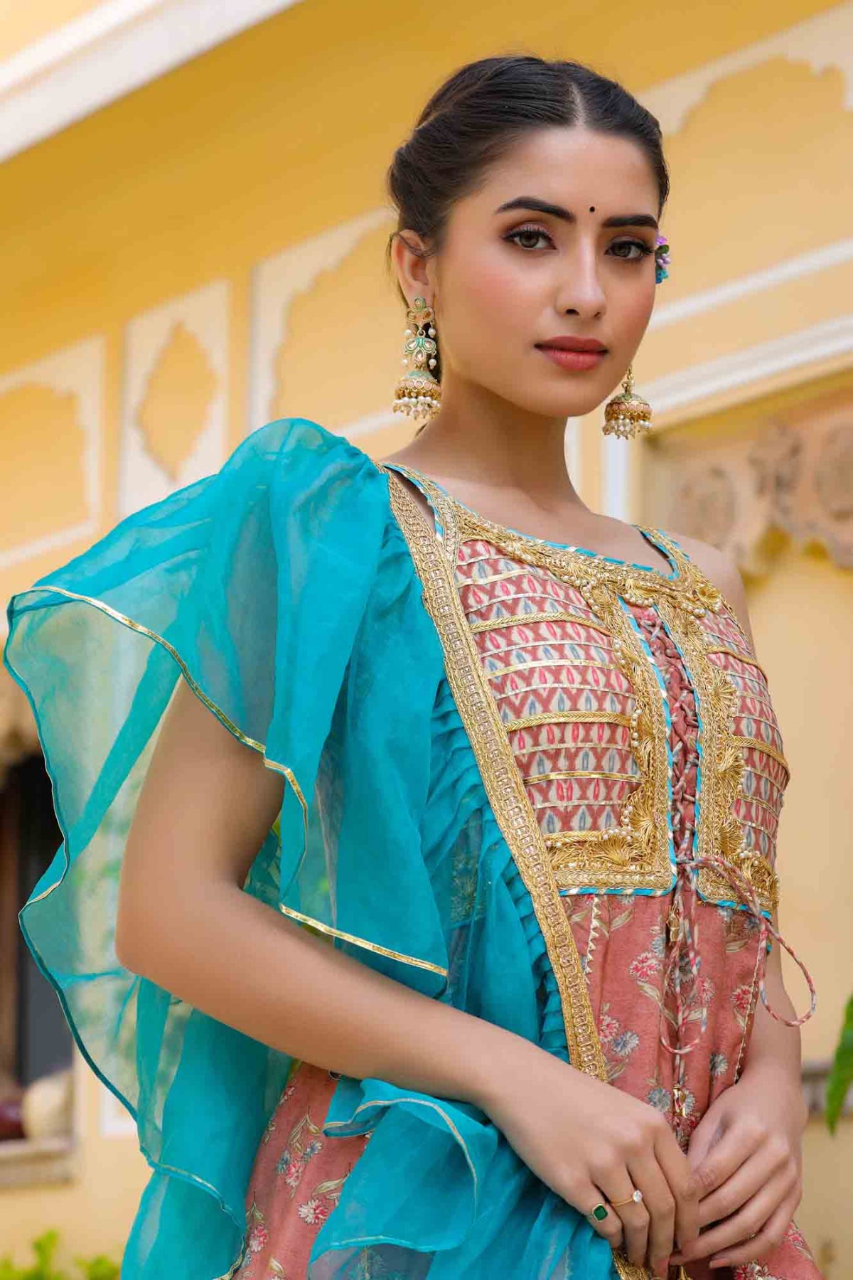 Woman wearing a traditional outfit with a turquoise dupatta and pink embroidered blouse.