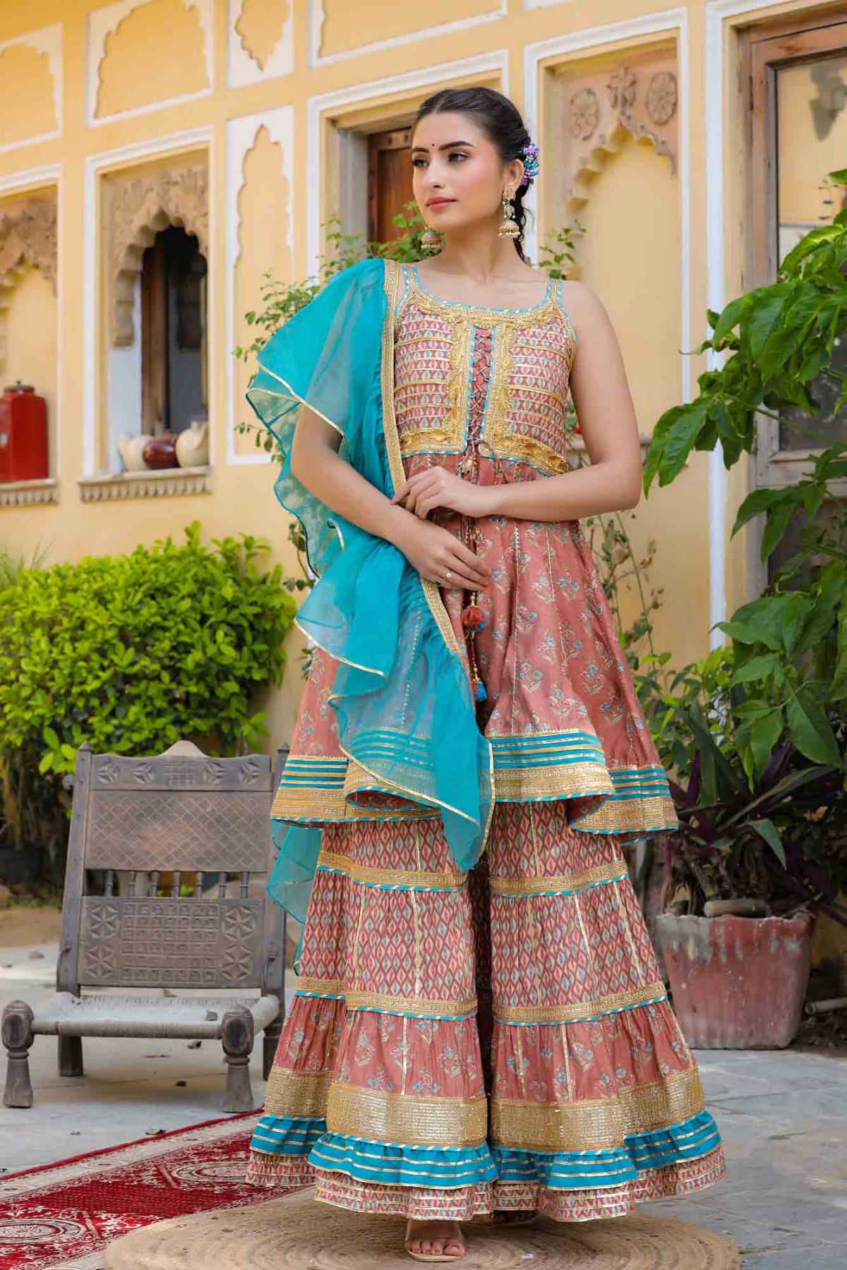 Woman in traditional outfit with blue dupatta standing outdoors.