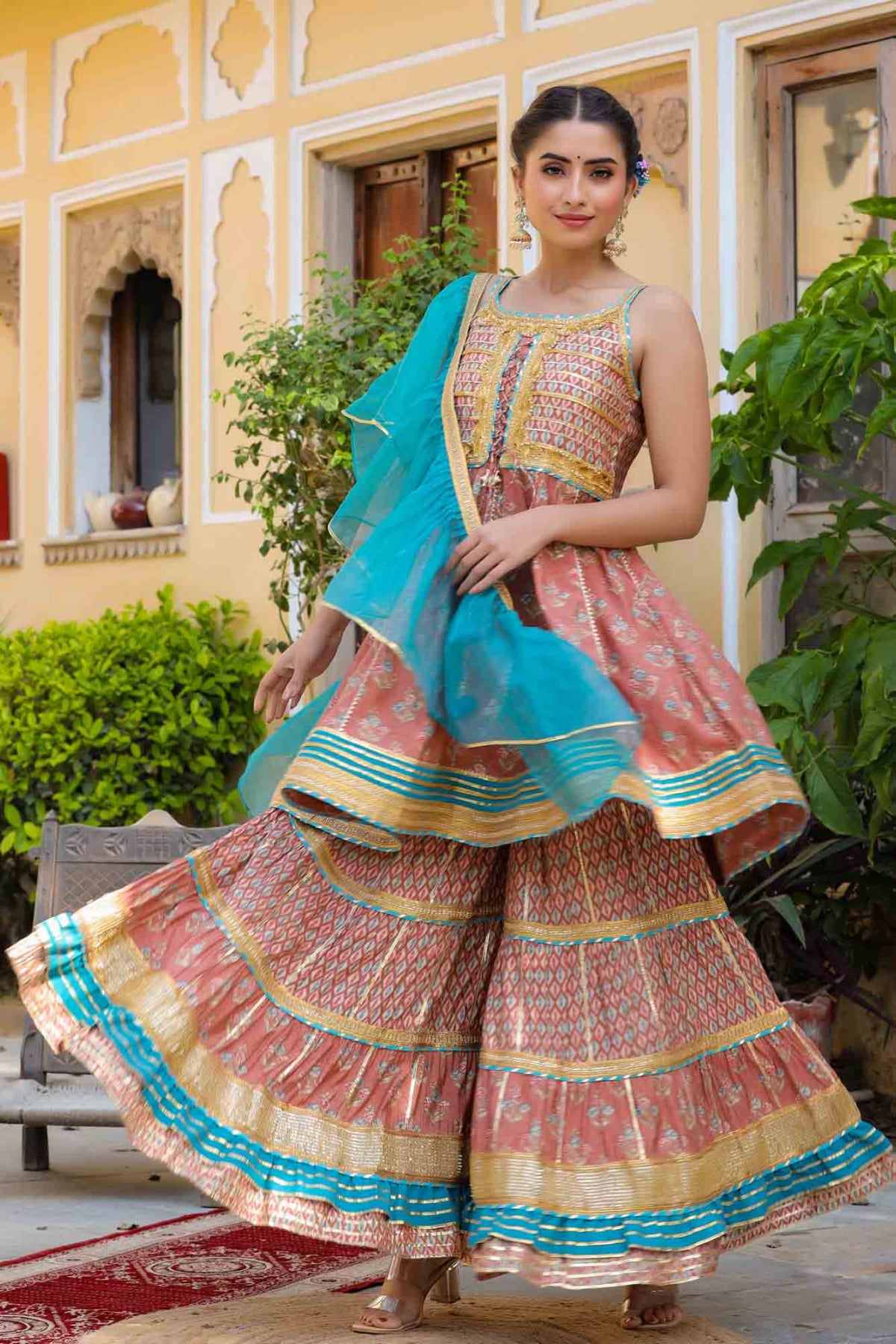 Woman in a traditional outfit with a colorful dress and blue dupatta standing outdoors.