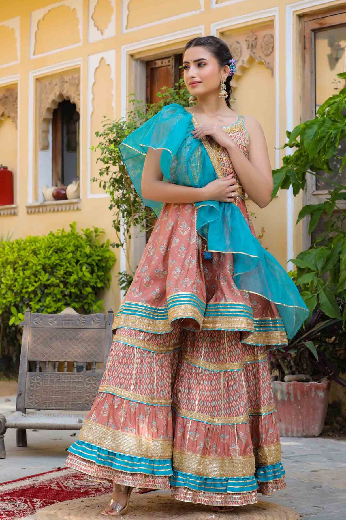 Woman in a traditional outfit with a blue dupatta standing outdoors.