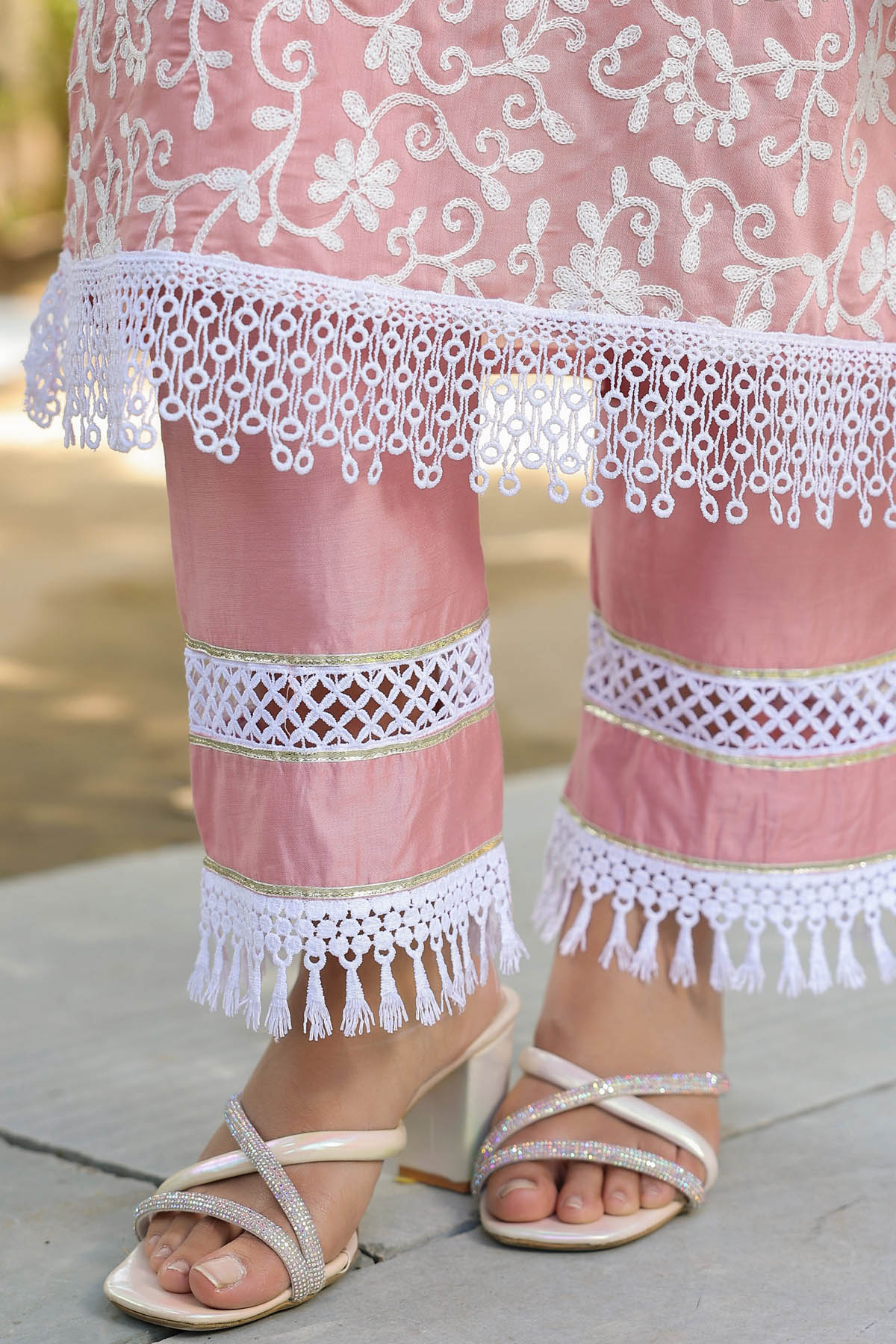 Pink embroidered garment with white lace details and sandals on a blurred background