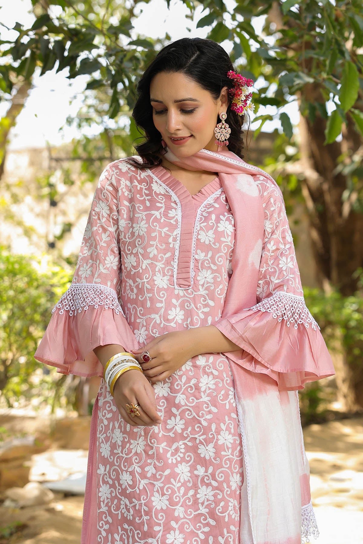 Woman wearing a pink and white embroidered traditional outfit with a green outdoor background