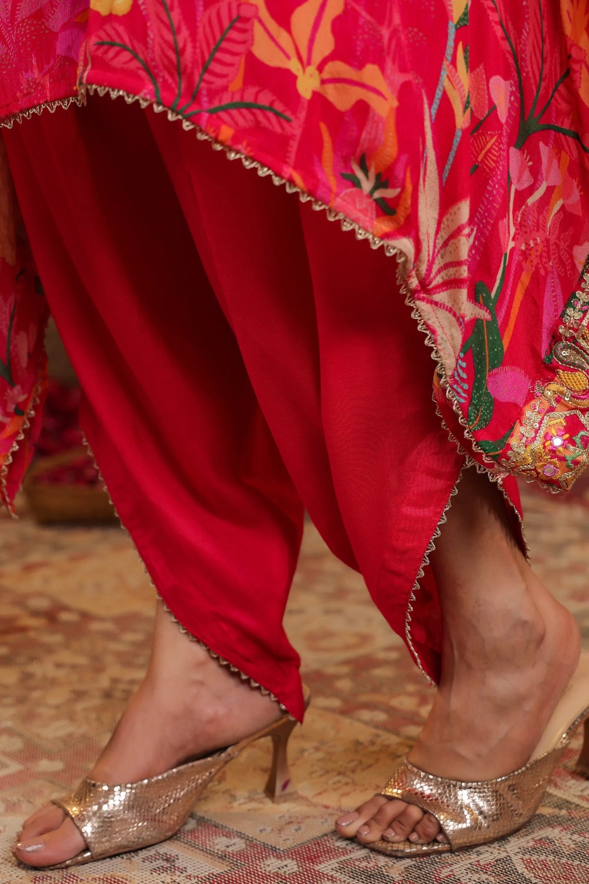 Red traditional outfit with floral patterns and gold high-heeled shoes on a patterned floor.