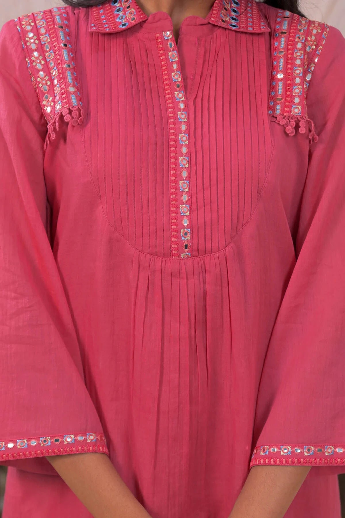 Close-up of a pink traditional outfit with intricate embroidery on a plain background