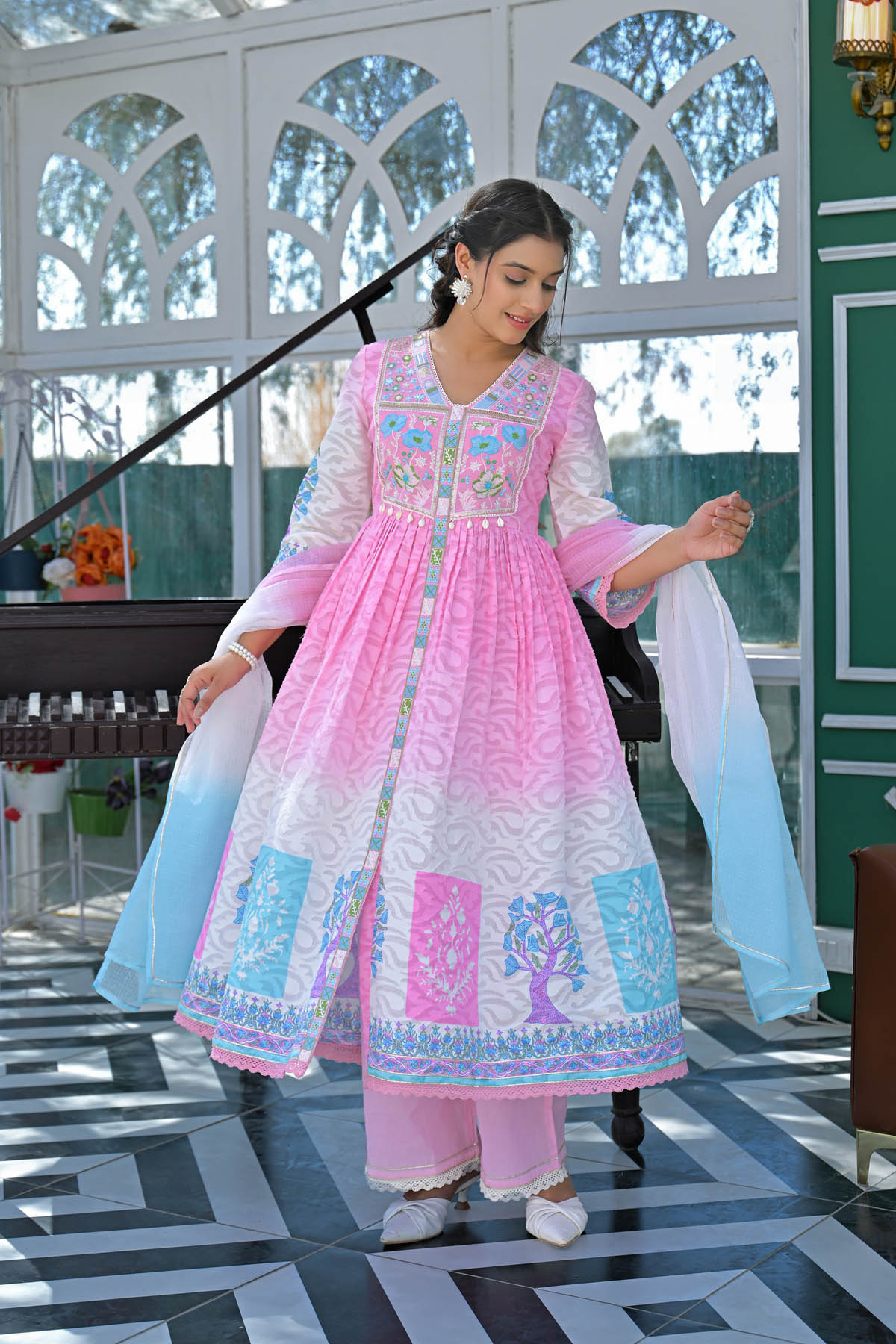 Woman in a pink and white traditional outfit with embroidery, standing indoors.
