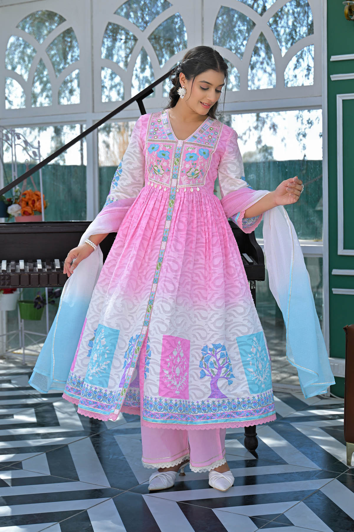 Woman in a pink and white traditional outfit with embroidery, standing indoors.