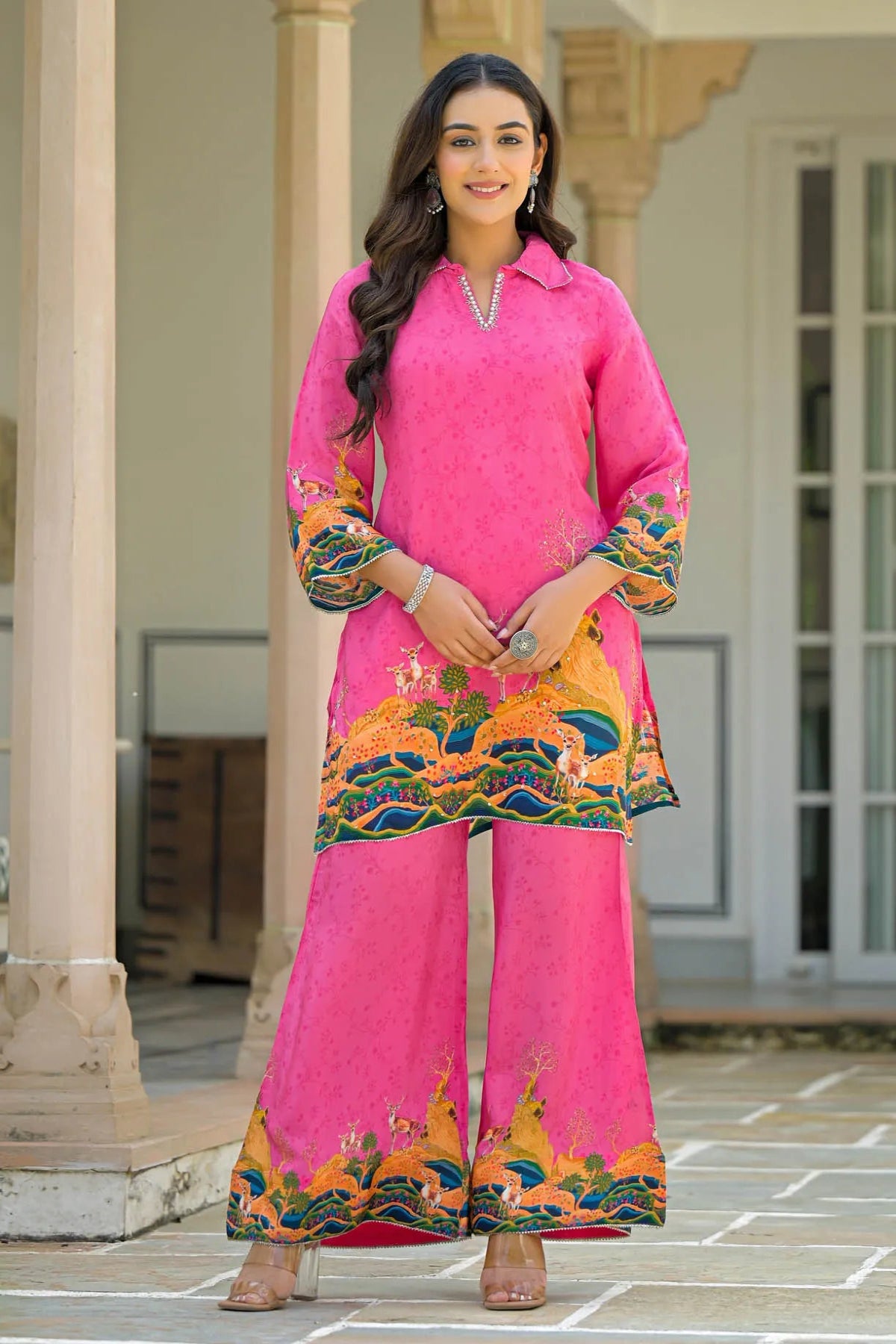 Woman wearing a bright pink traditional outfit with colorful patterns in an outdoor setting.