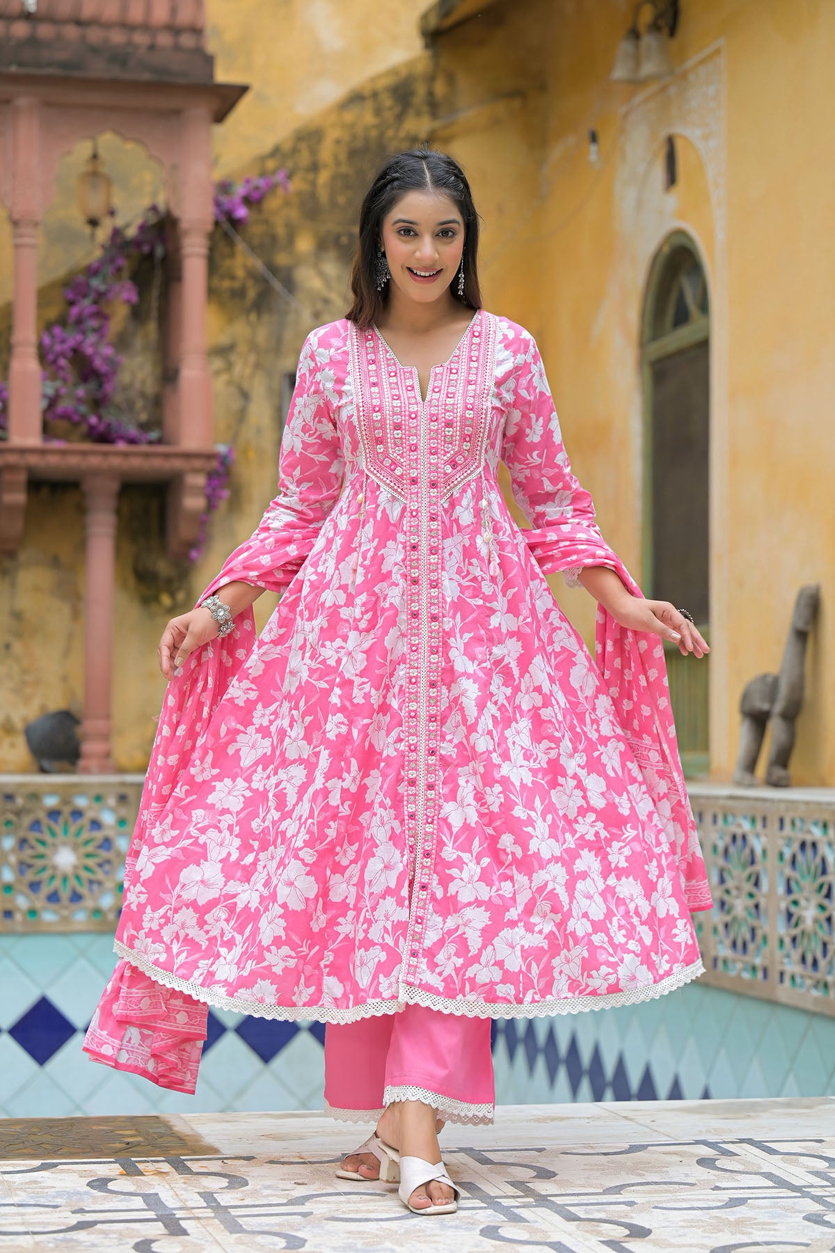 Woman in a pink traditional outfit standing in front of a decorative wall.