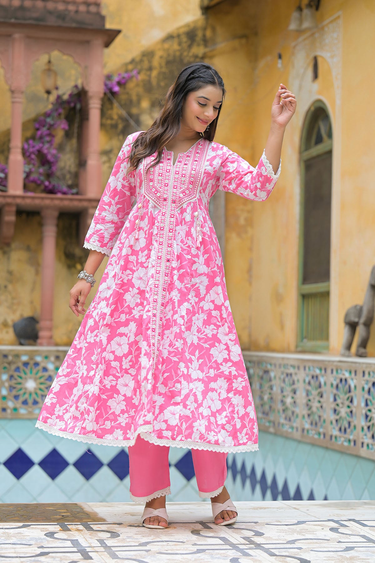 Woman in a pink floral dress standing in front of a decorative building.