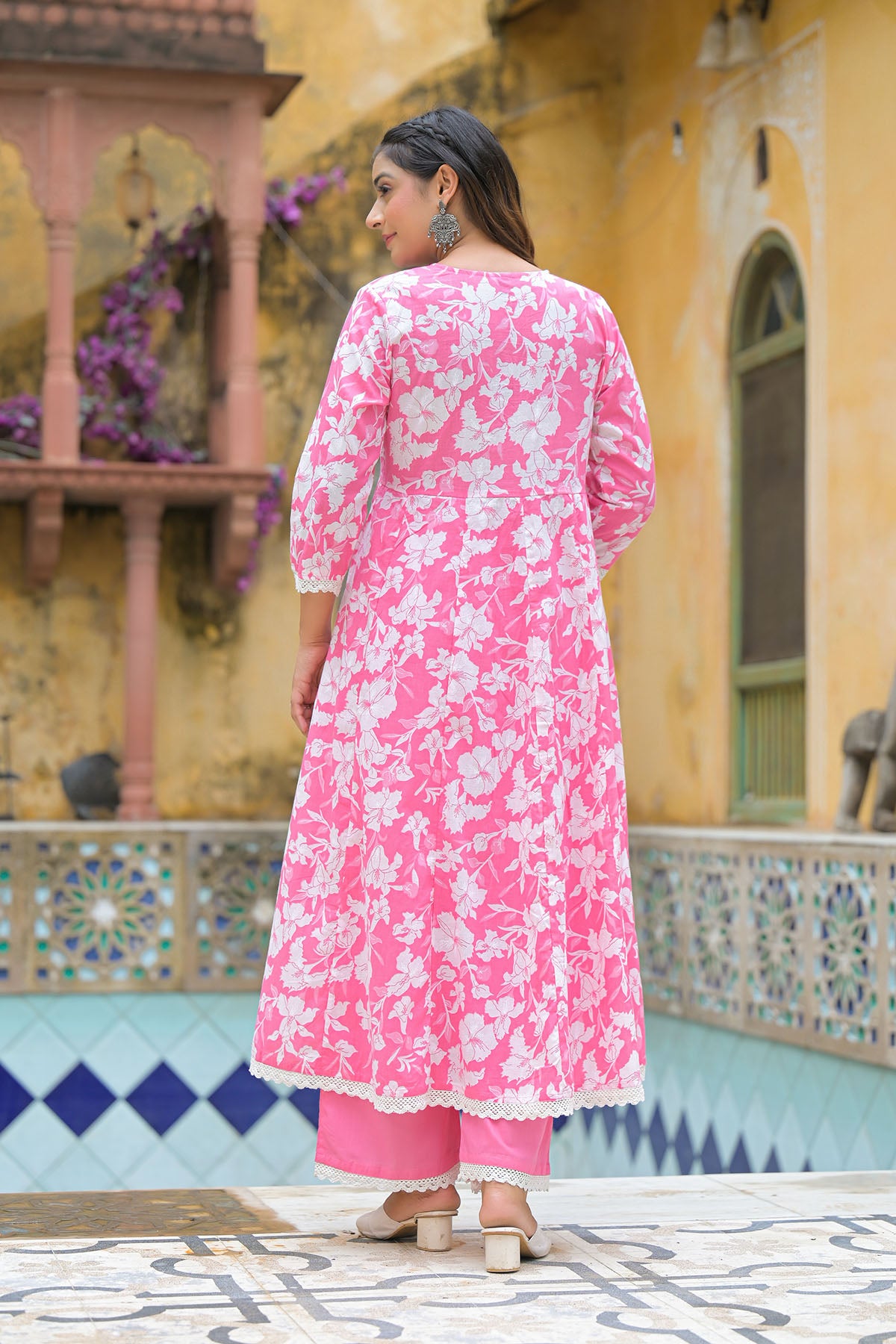 Woman wearing a pink floral dress standing in front of a colorful building.