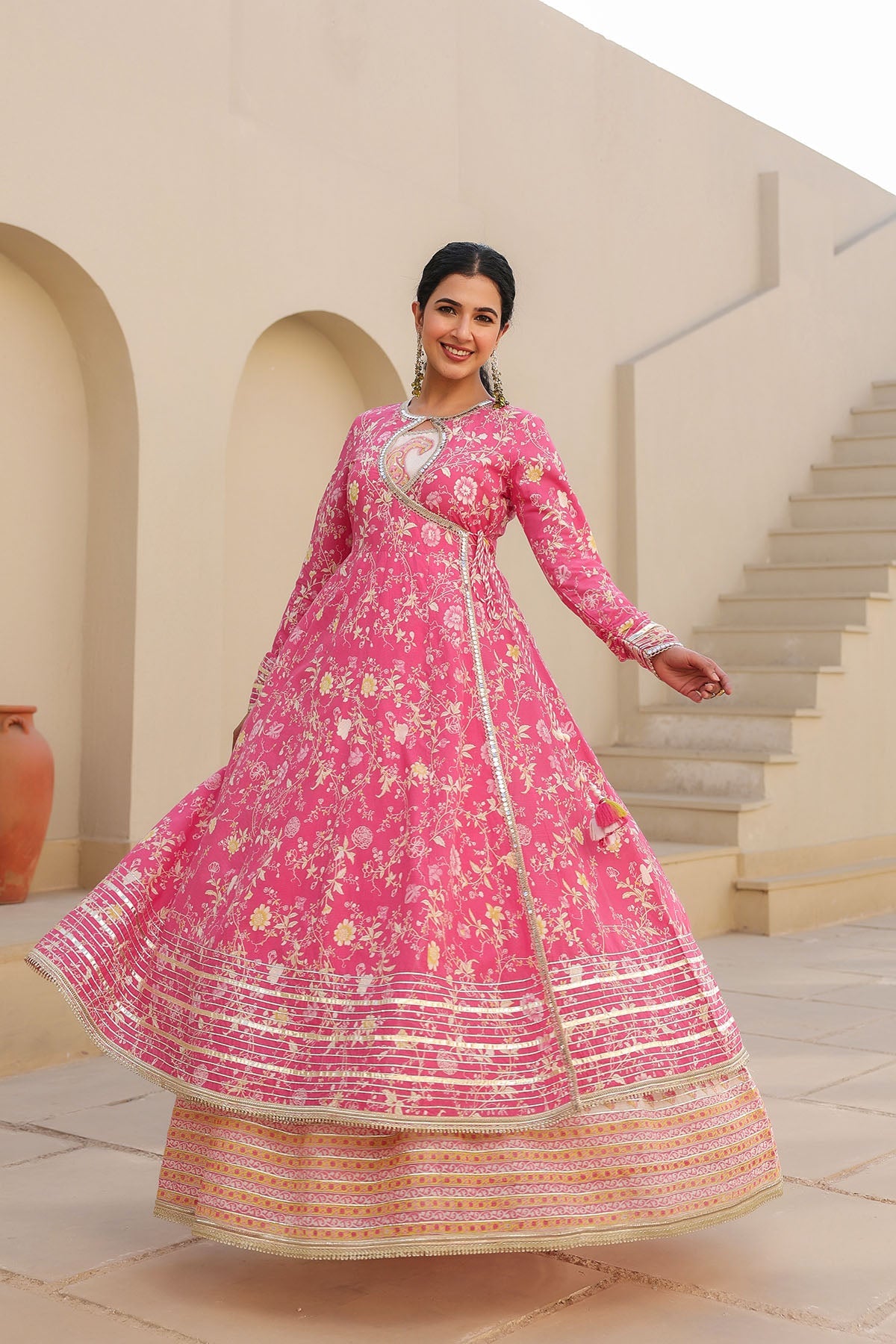 Woman in a pink traditional outfit standing in front of a beige building with arches.