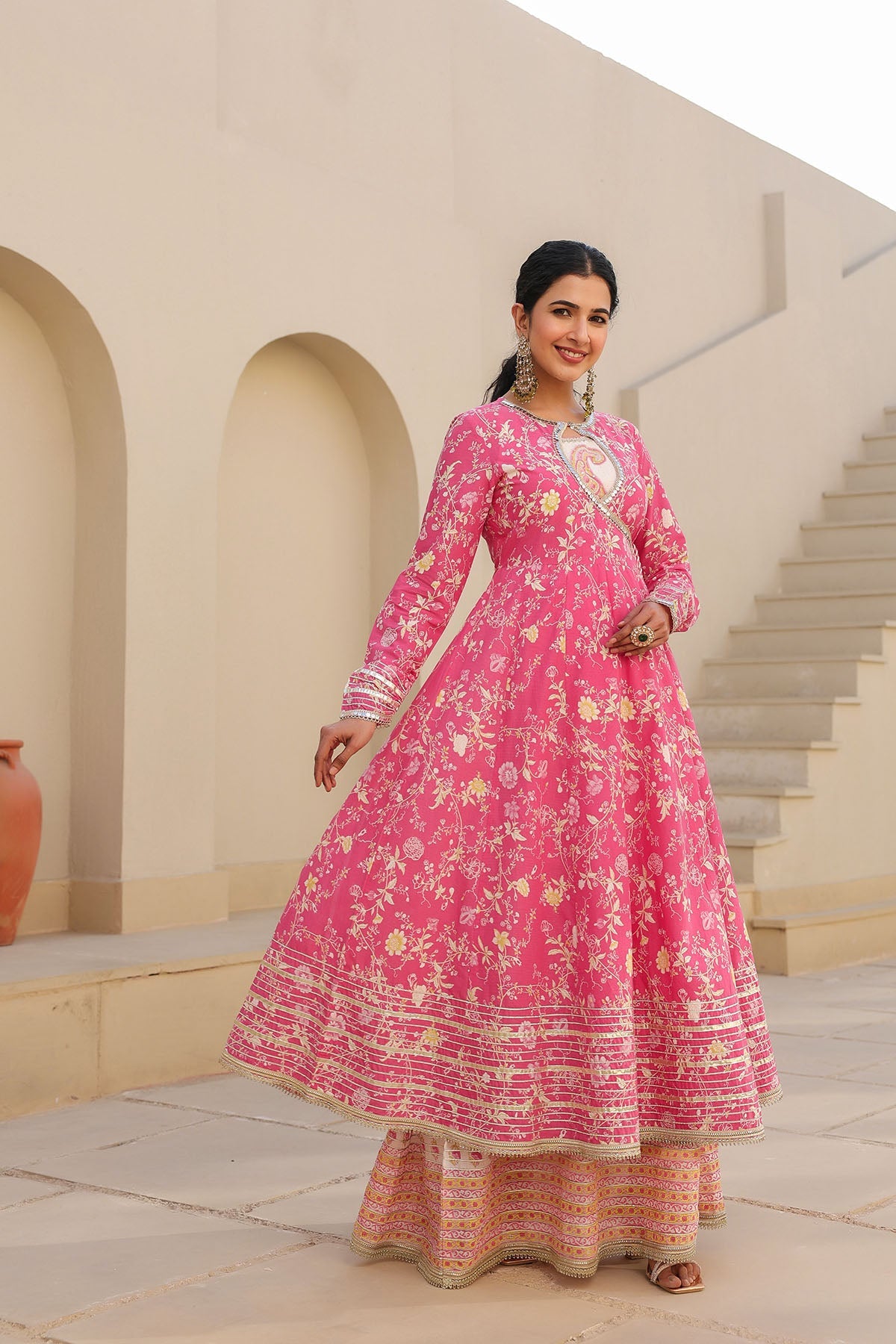 Woman in a pink traditional outfit standing outdoors with architectural background