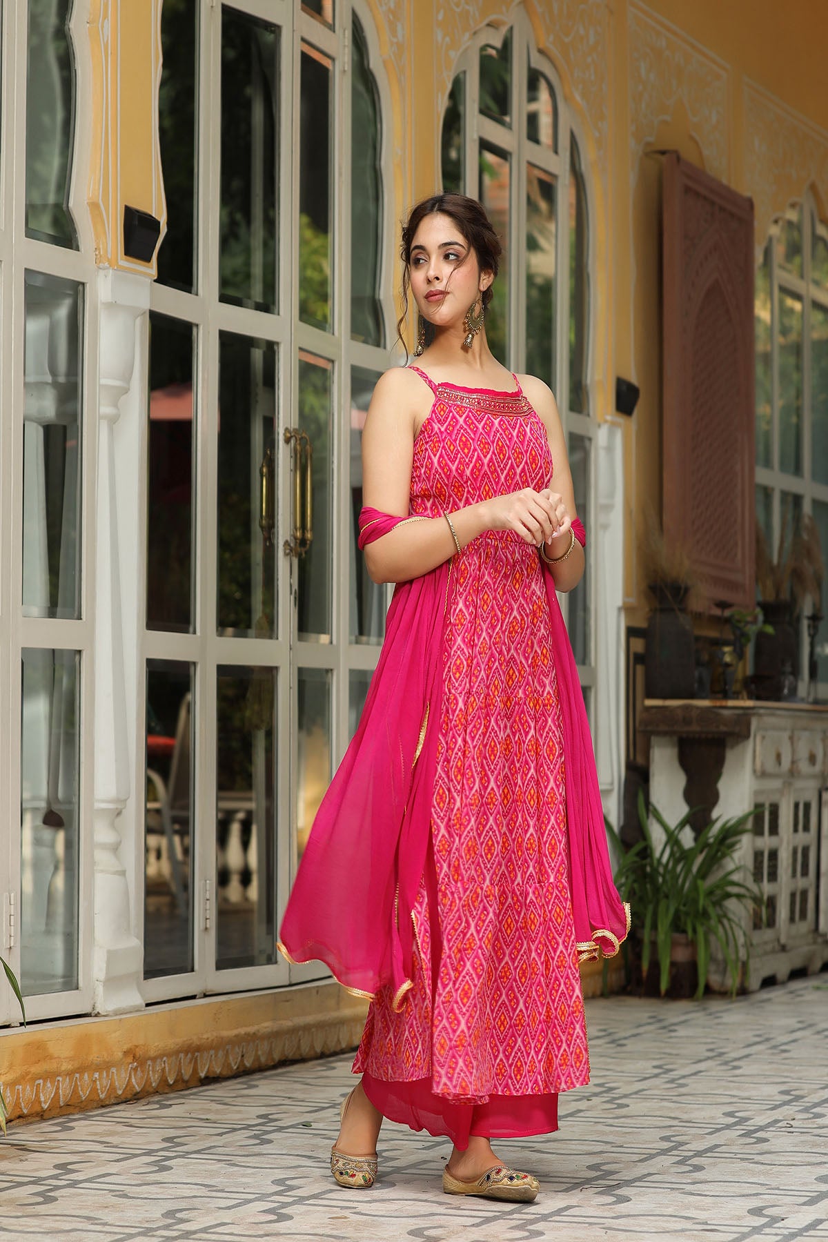 Woman in a pink traditional outfit standing in front of a decorative door.