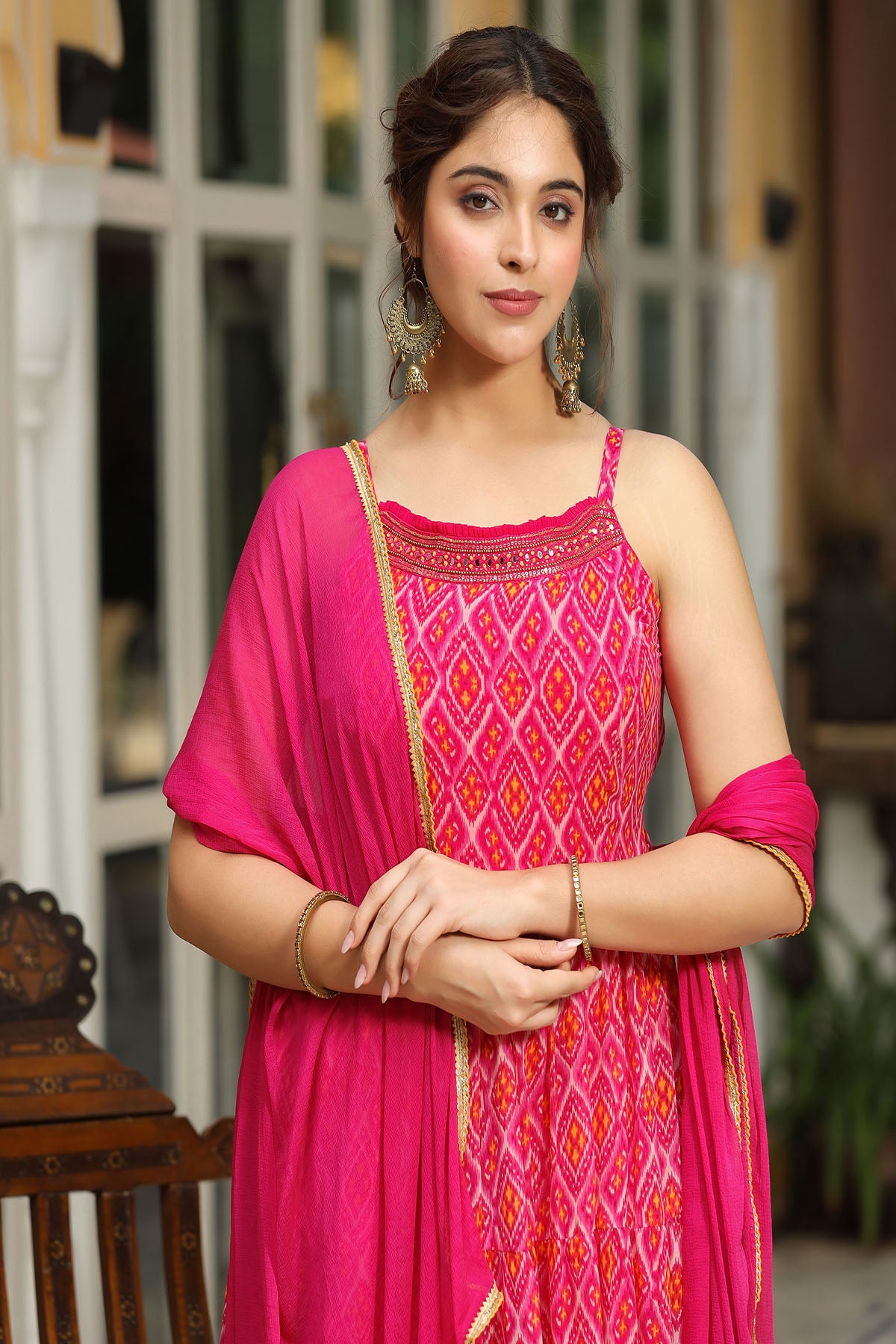 Woman wearing a pink traditional outfit with intricate patterns, standing indoors.
