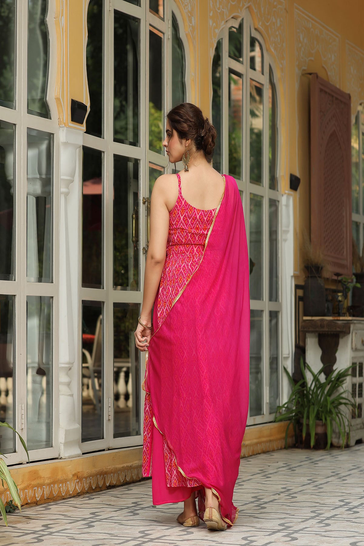 Woman in a bright pink saree with red patterns standing in front of a building with large windows.