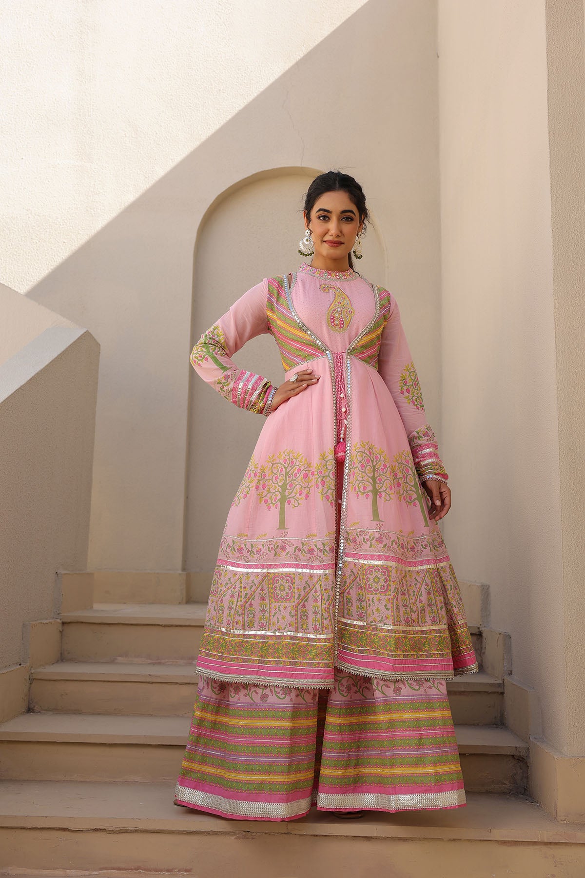 Woman wearing a traditional pink outfit with intricate patterns on a light background