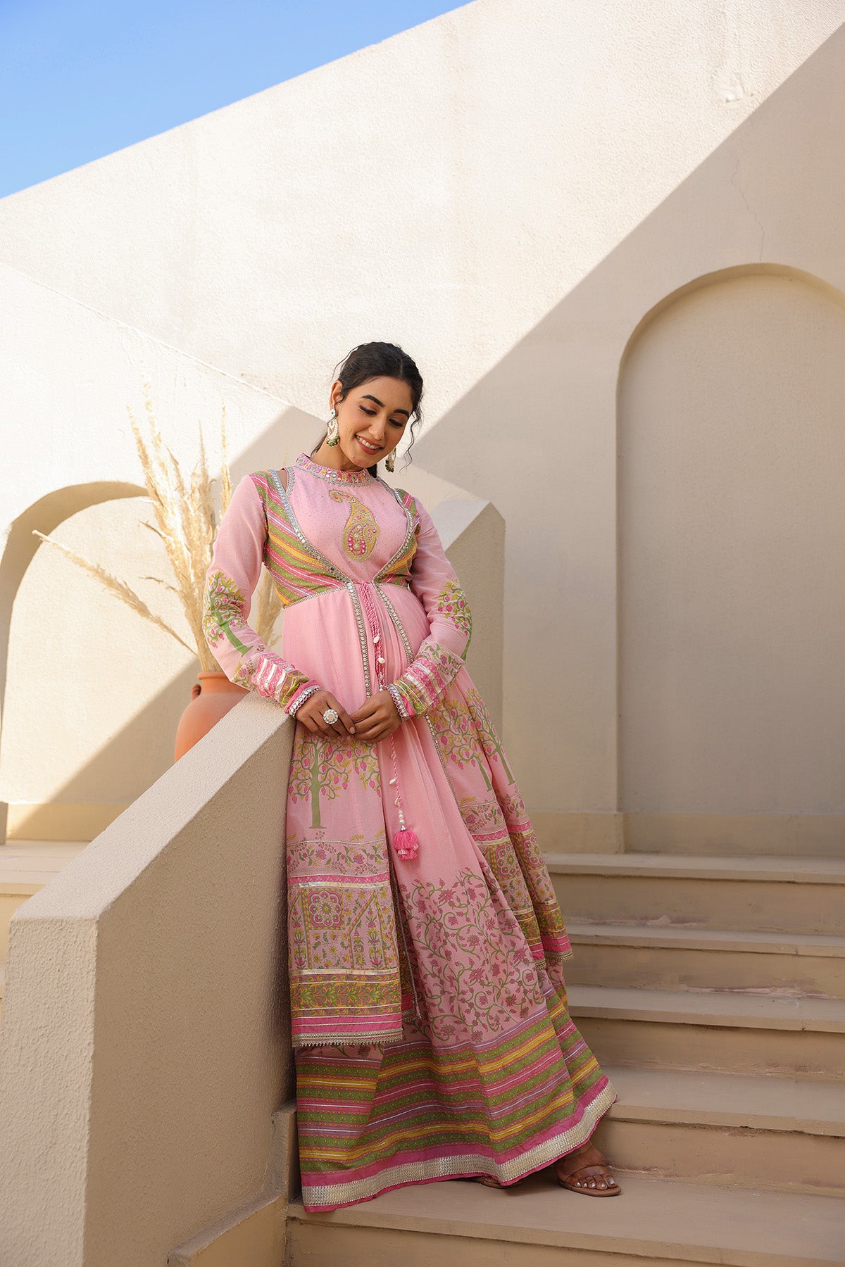 Woman in a pink traditional outfit standing on steps with a white architectural background