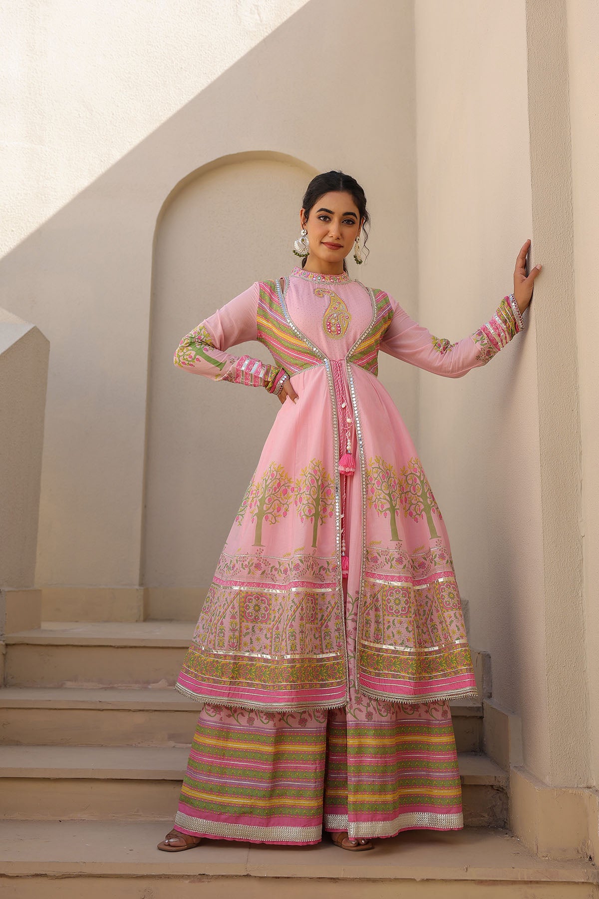 Woman in a traditional pink and gold outfit standing on steps with a neutral background