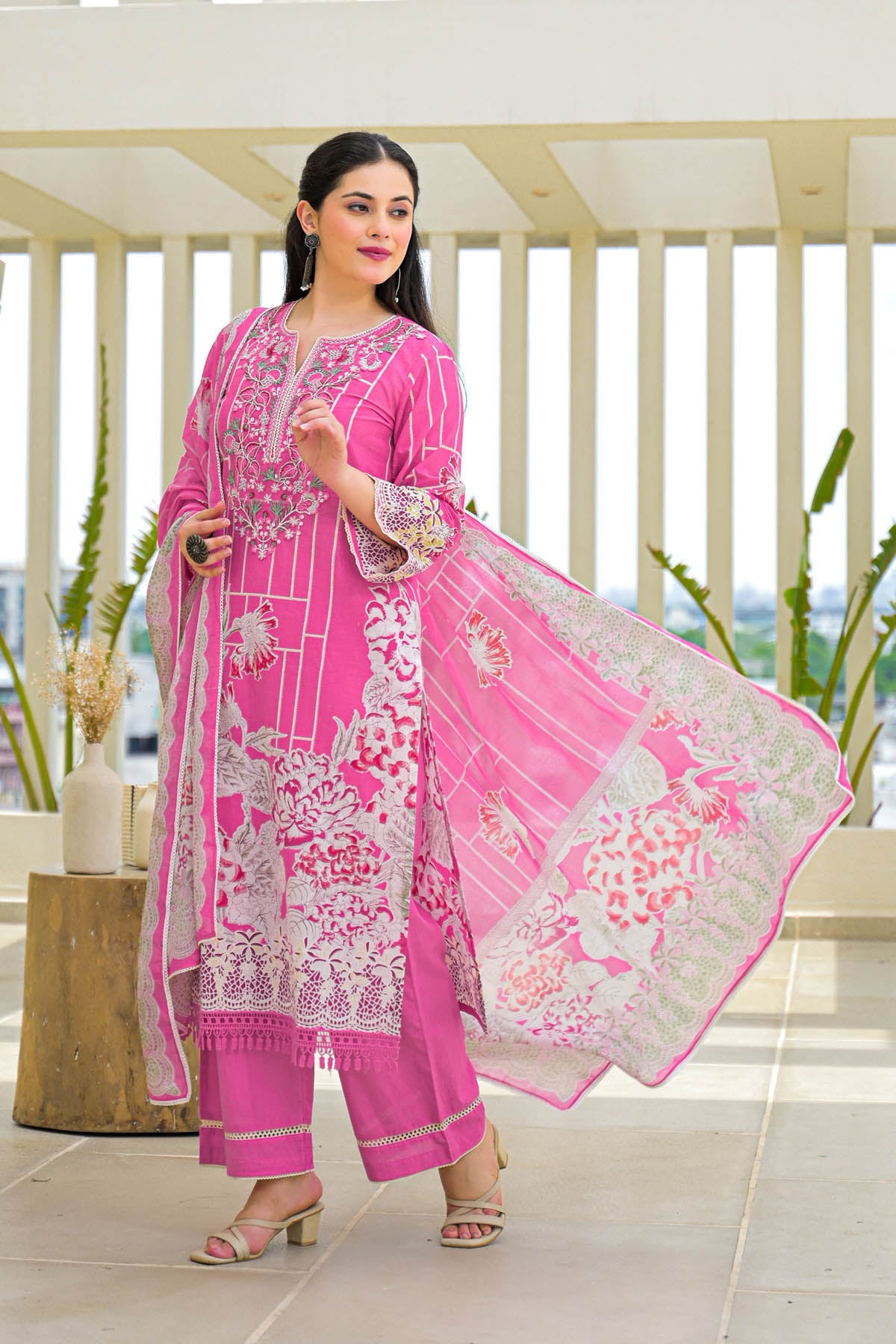 Woman in a pink traditional outfit with white embroidery indoors.