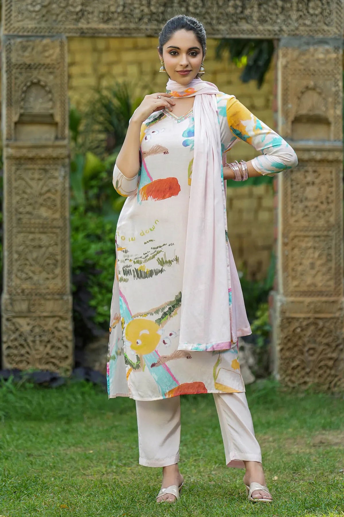 Woman in a colorful traditional outfit standing in front of an ornate stone wall.