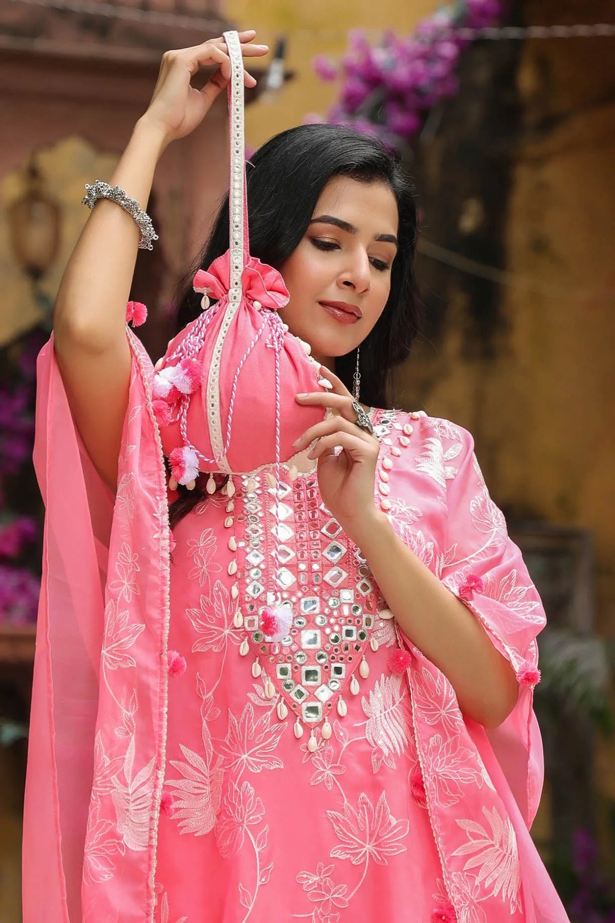 Woman in a pink traditional outfit with intricate designs, holding a measuring tape.
