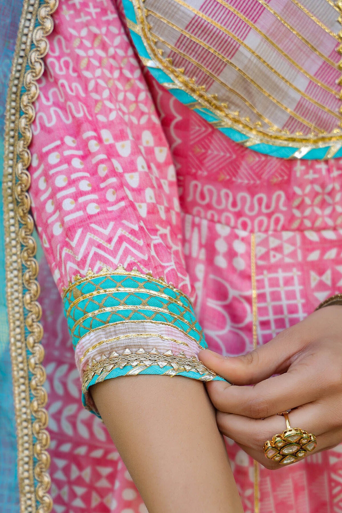 Close-up of a pink saree with gold and green border, held by a hand.