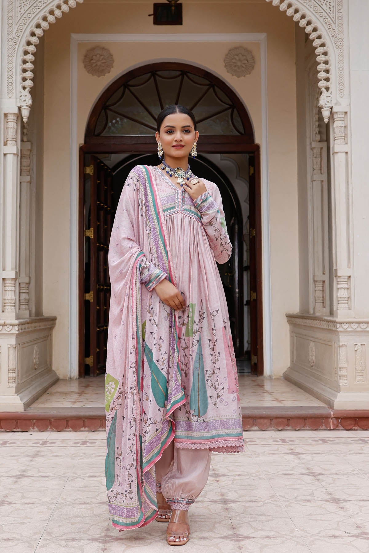 Woman in a traditional pink outfit standing in front of an archway.