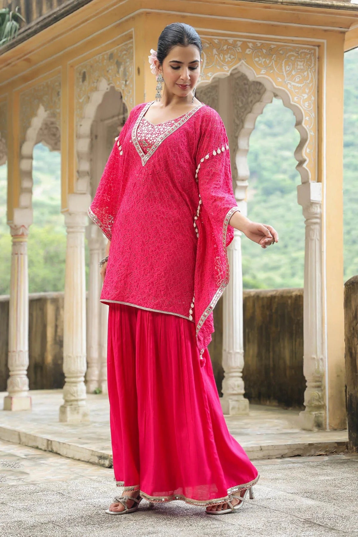 Woman in a pink traditional outfit standing in front of an architectural structure with greenery in the background