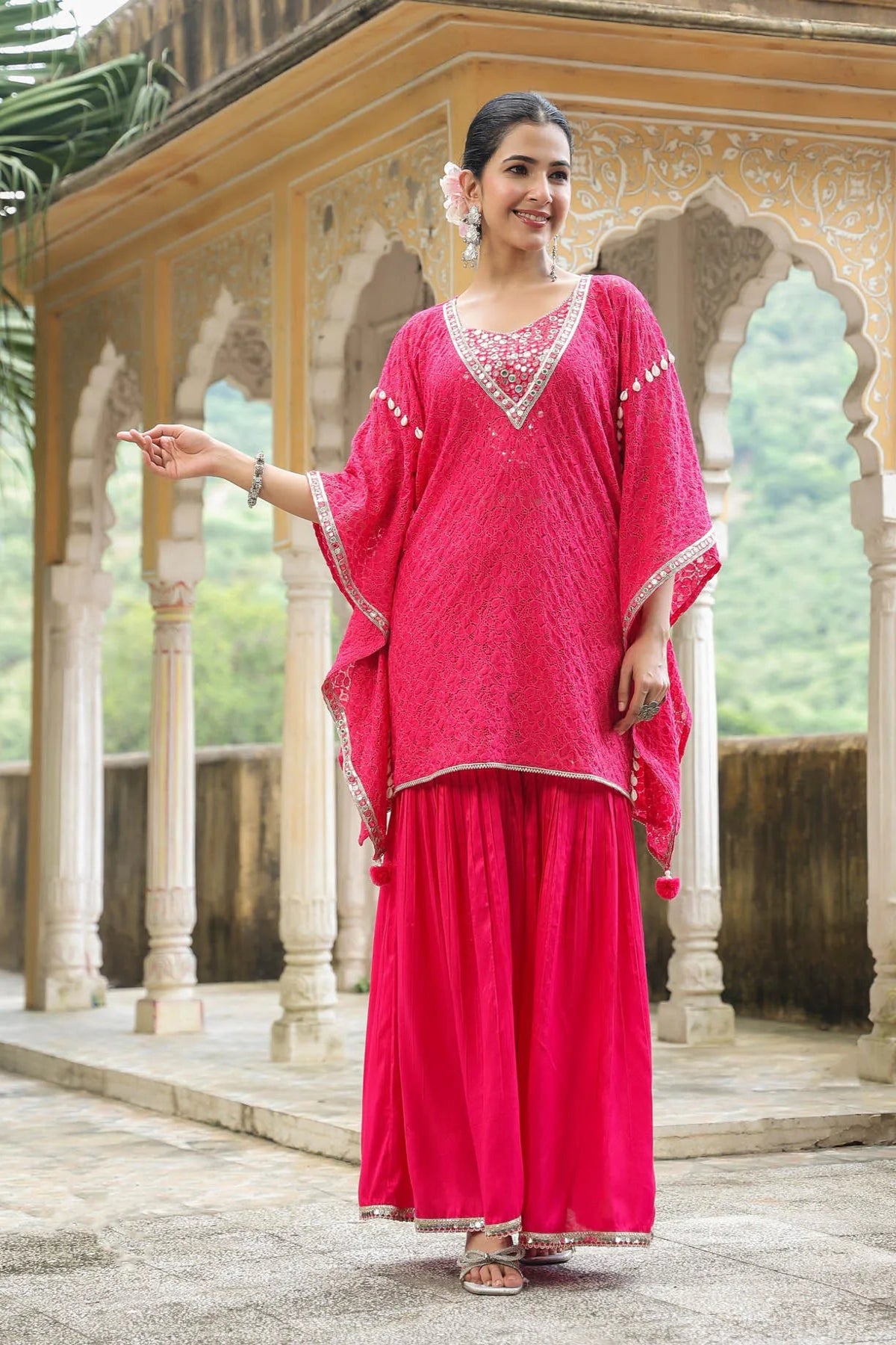 Woman in a bright pink traditional outfit standing in front of an architectural structure.